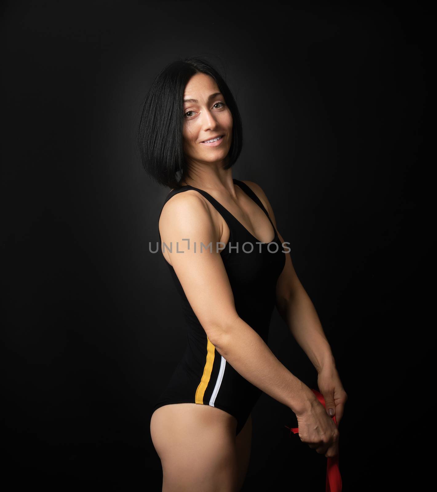 young woman gymnast of Caucasian appearance with black hair spins red satin ribbons, gymnastic exercises on black background