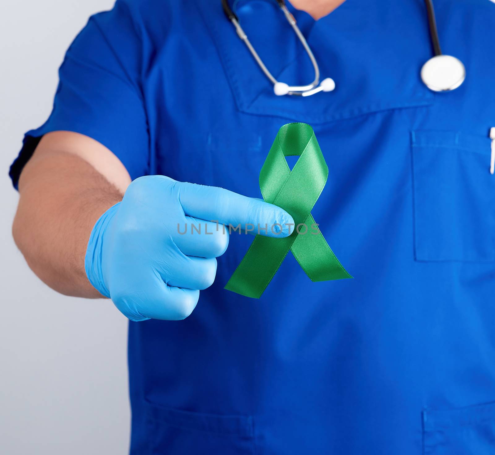 doctor in blue uniform and latex gloves holds a green ribbon as a symbol of early research and disease control, symbol of Lyme disease, kidney transplantation and organ donation