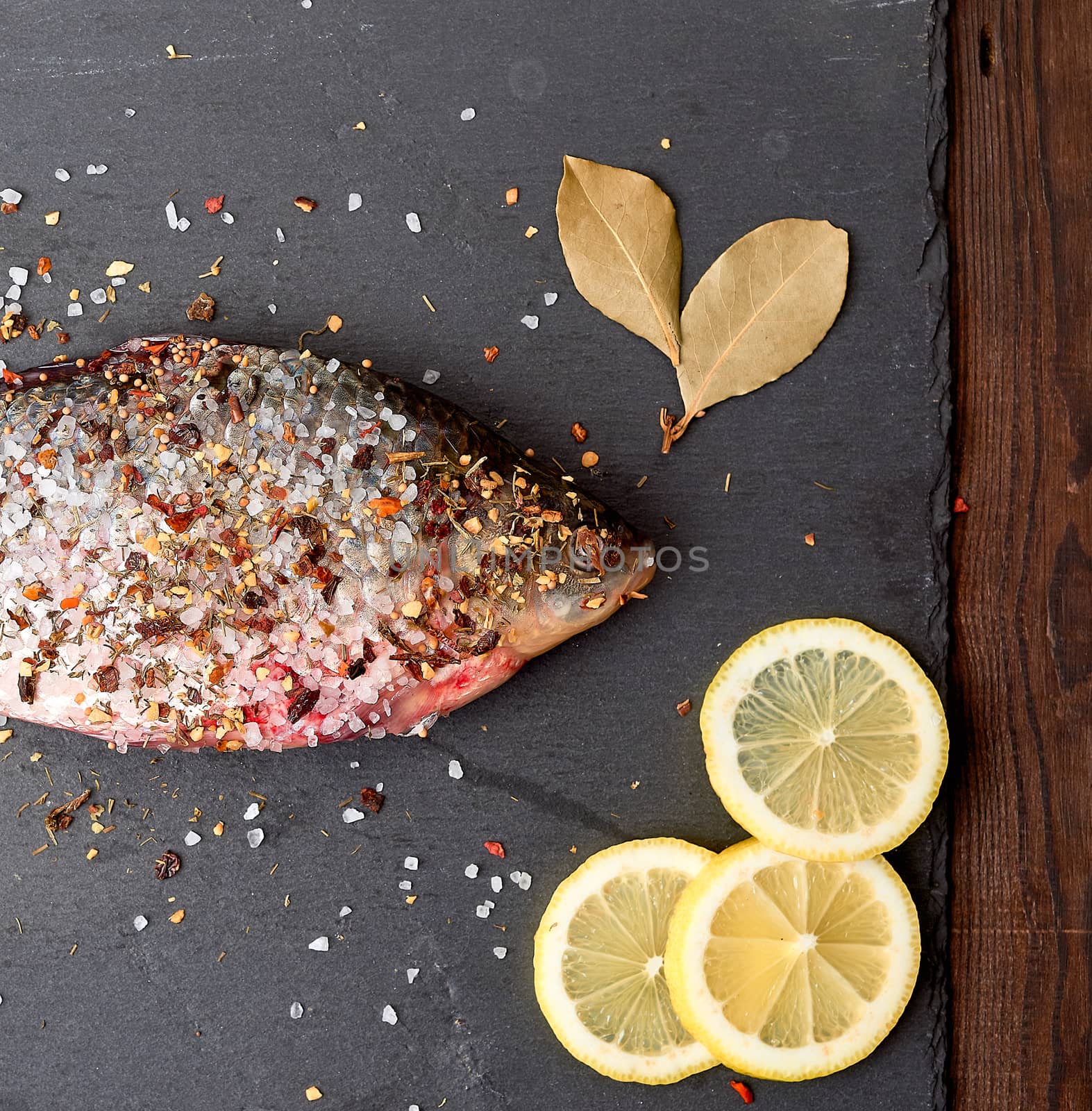 head of fresh crucian fish sprinkled with spices lies on a black slate board, top view