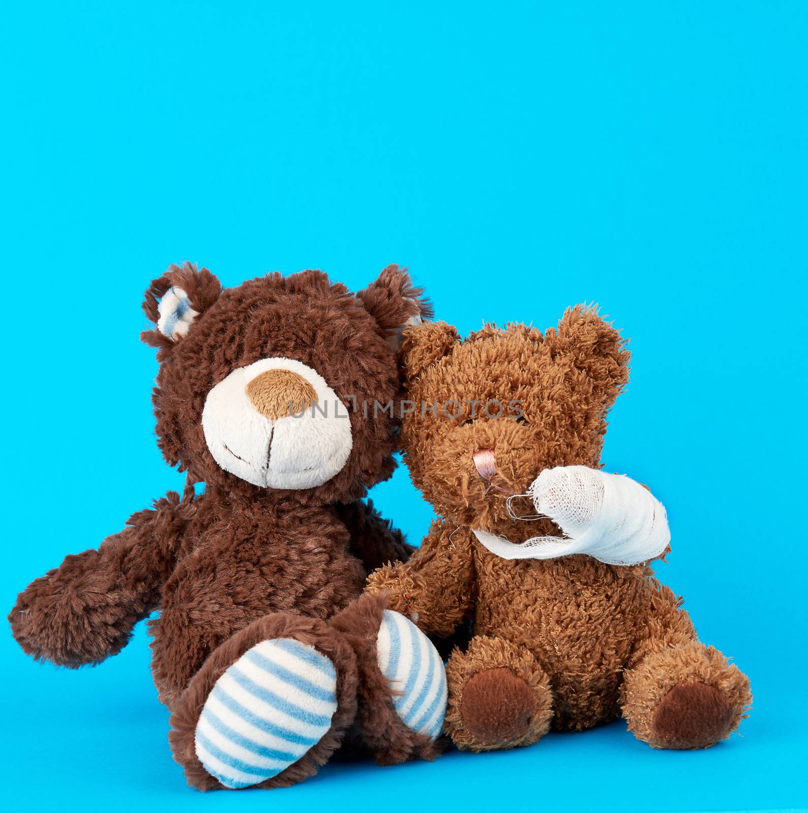 brown teddy bear with rewound white bandage paw on a blue background, pediatrics concept