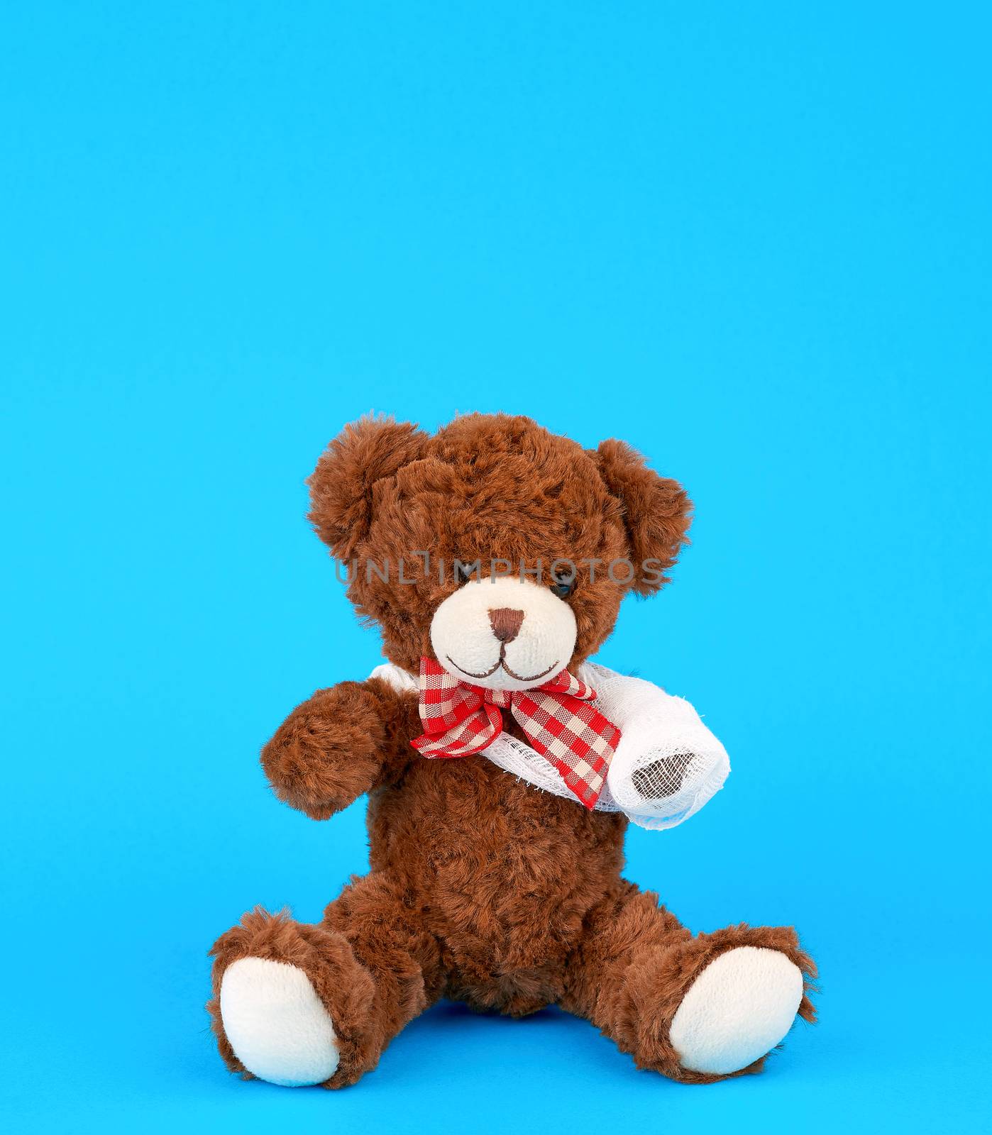 brown teddy bear with rewound white bandage paw on a blue background, pediatrics concept