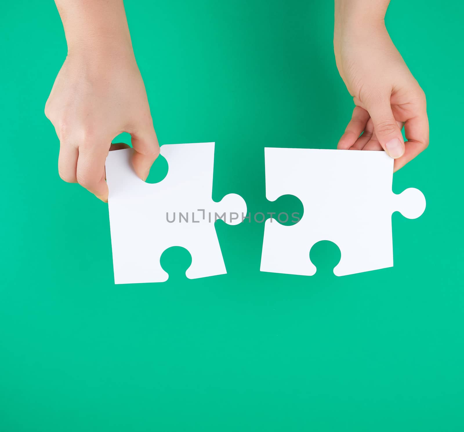 white big puzzles in female hand on green background, copy space