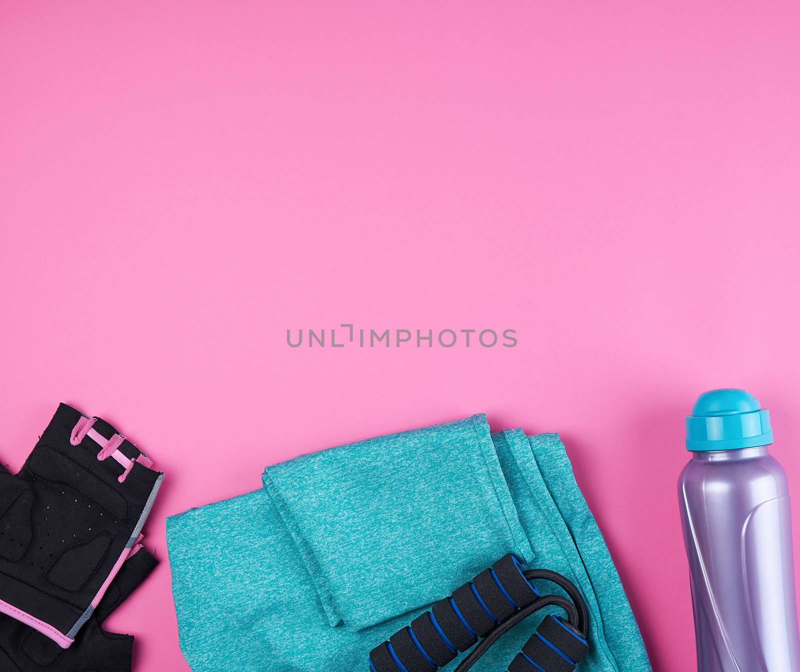 pink women's sneakers, bottle of water, gloves and a jump rope for sports on a pink background, top view, copy space