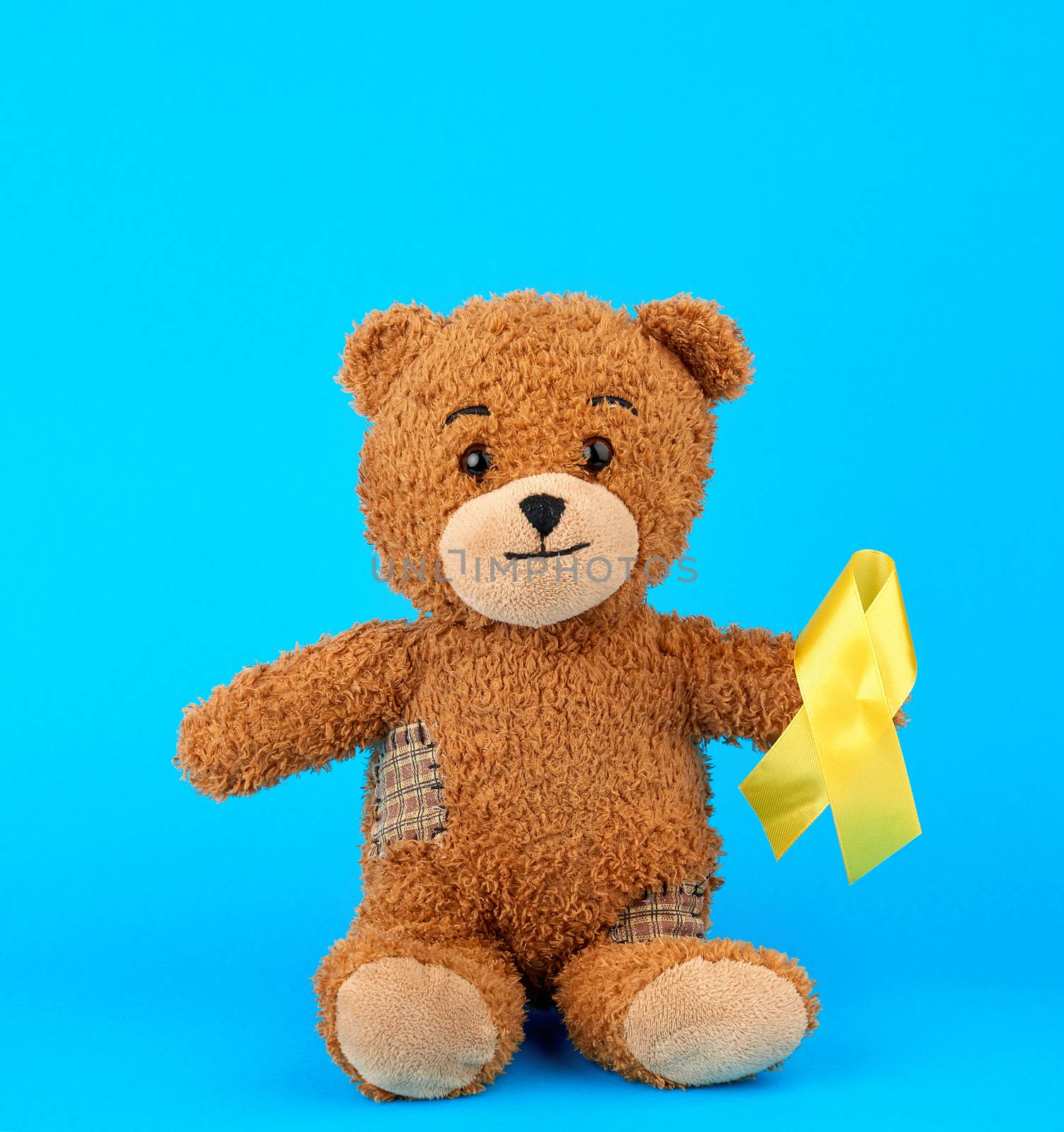 brown teddy bear sits and holds in his paw a yellow silk ribbon  by ndanko