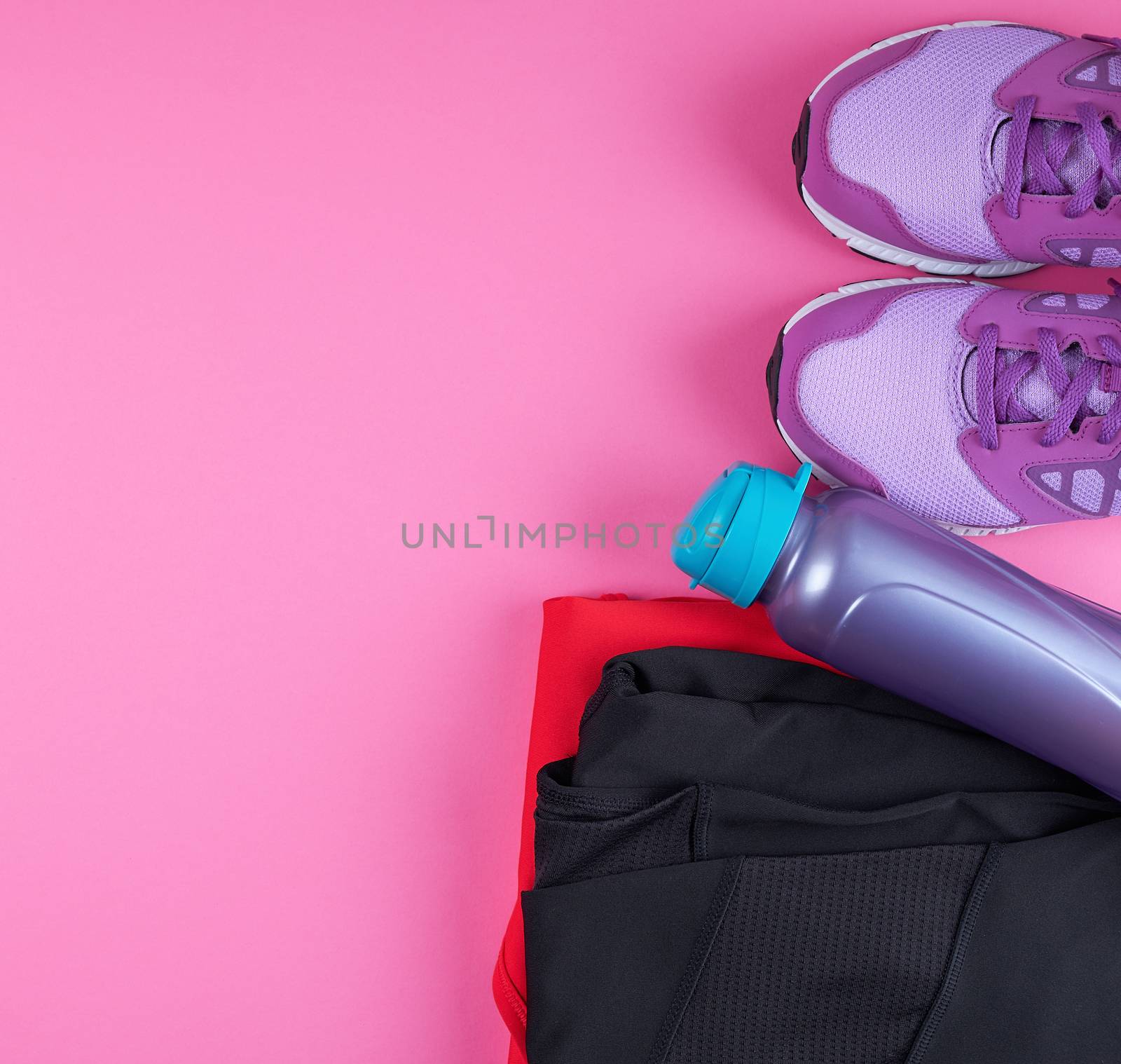 pink women's sneakers, bottle of water, clothes for sports on a pink background, top view, copy space