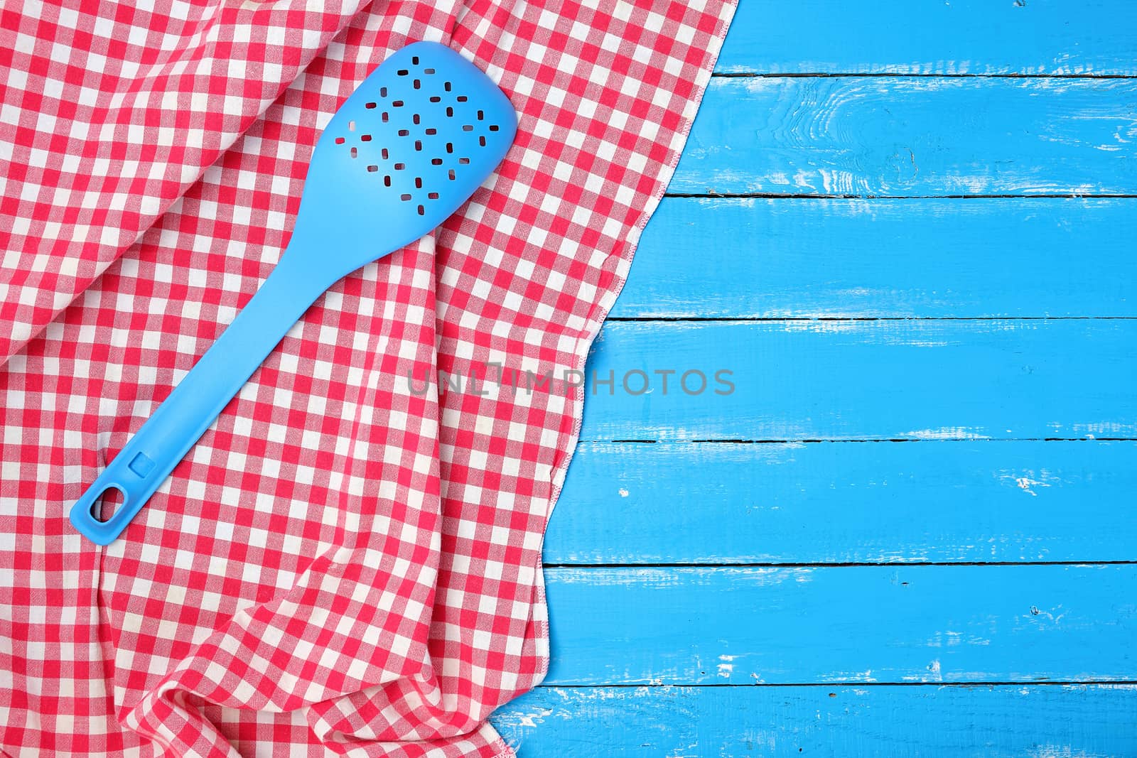plastic blue spoon with holes on a red textile napkin, wooden background
