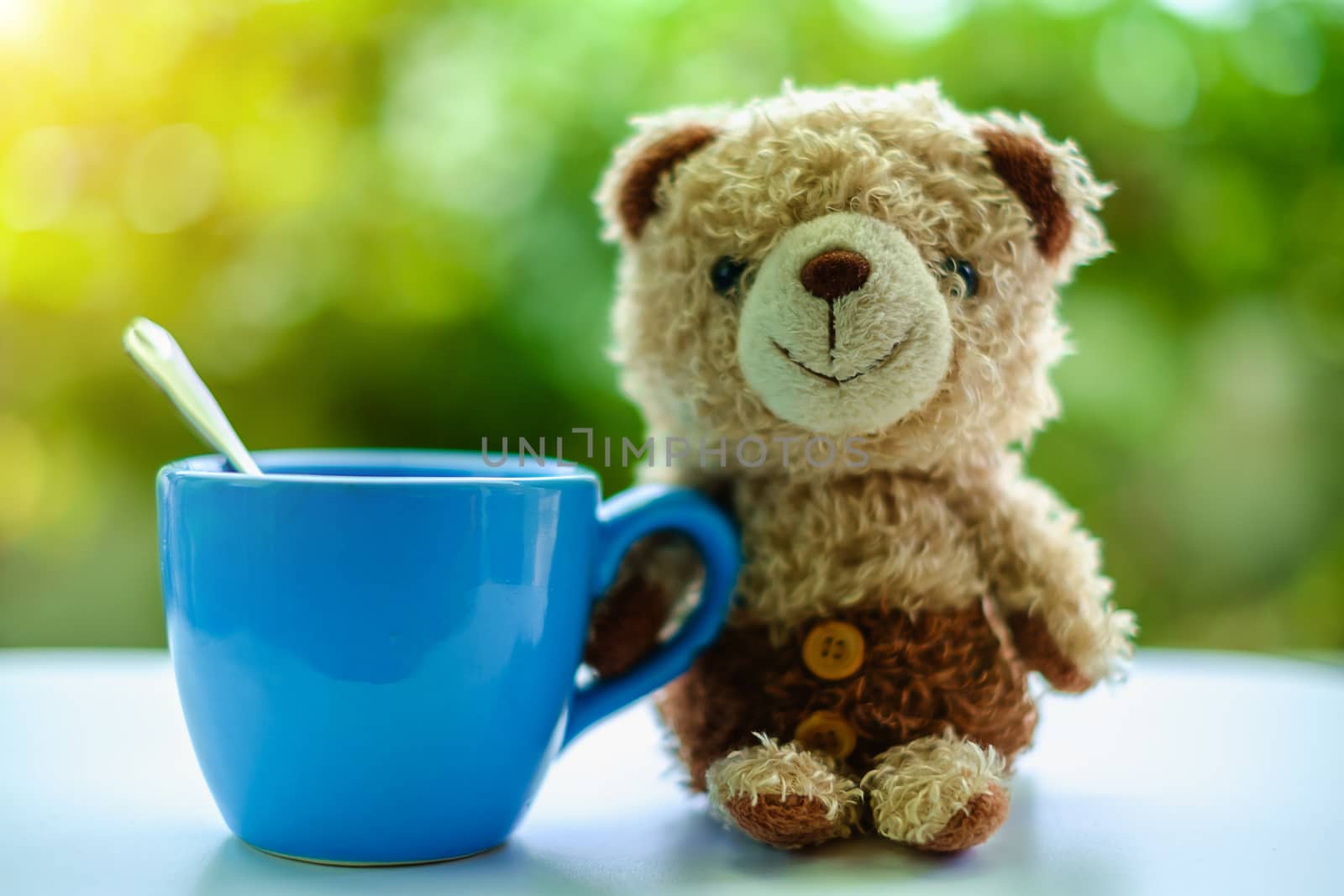 Brown bear doll sitting with a cup of coffee on blurred green natural background