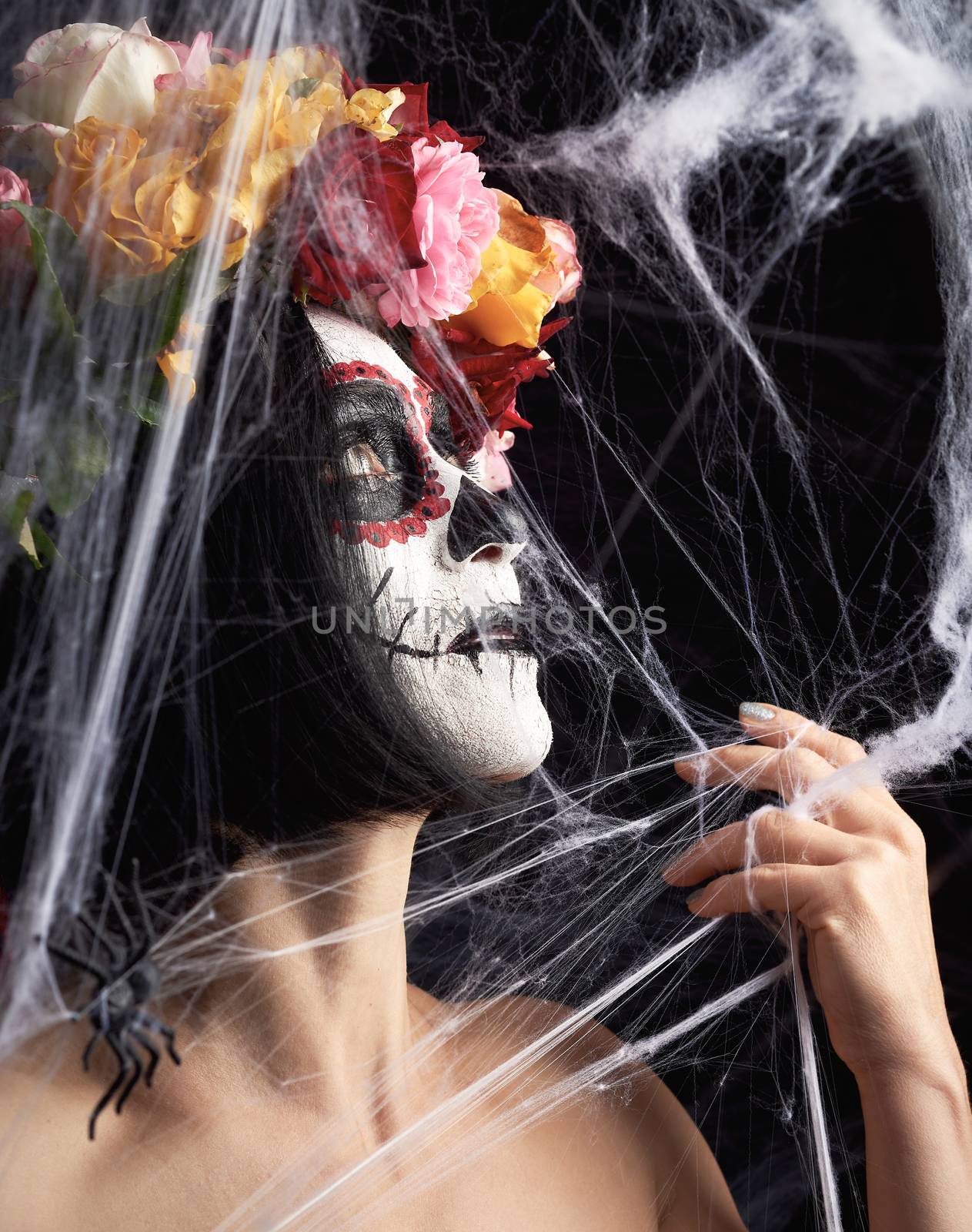 girl with black hair is dressed in a wreath of multi-colored roses and makeup is made on her face Sugar skull to the day of the Dead