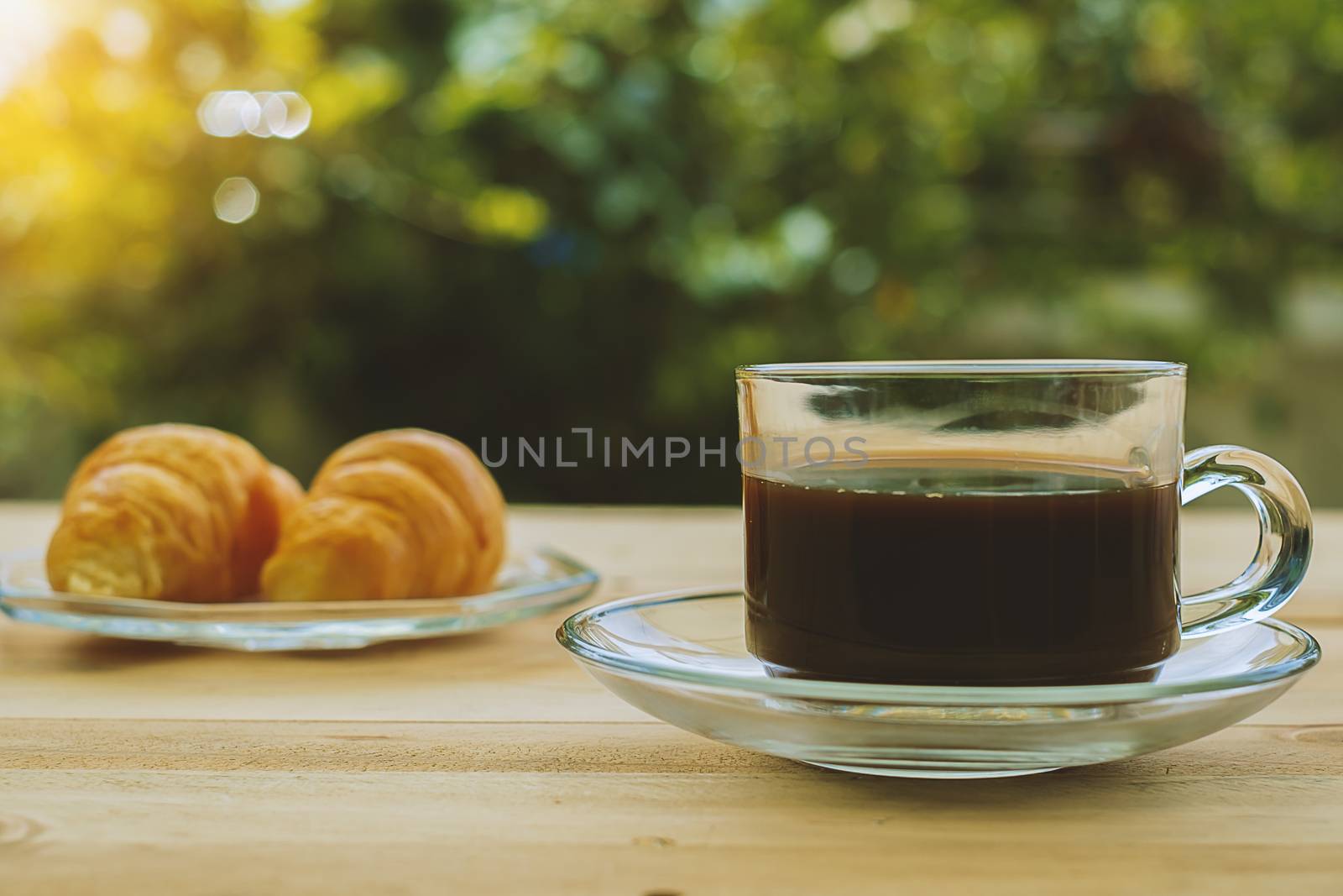 A cup of coffee and croissants on blurred green natural background, selective focus and vintage retro color