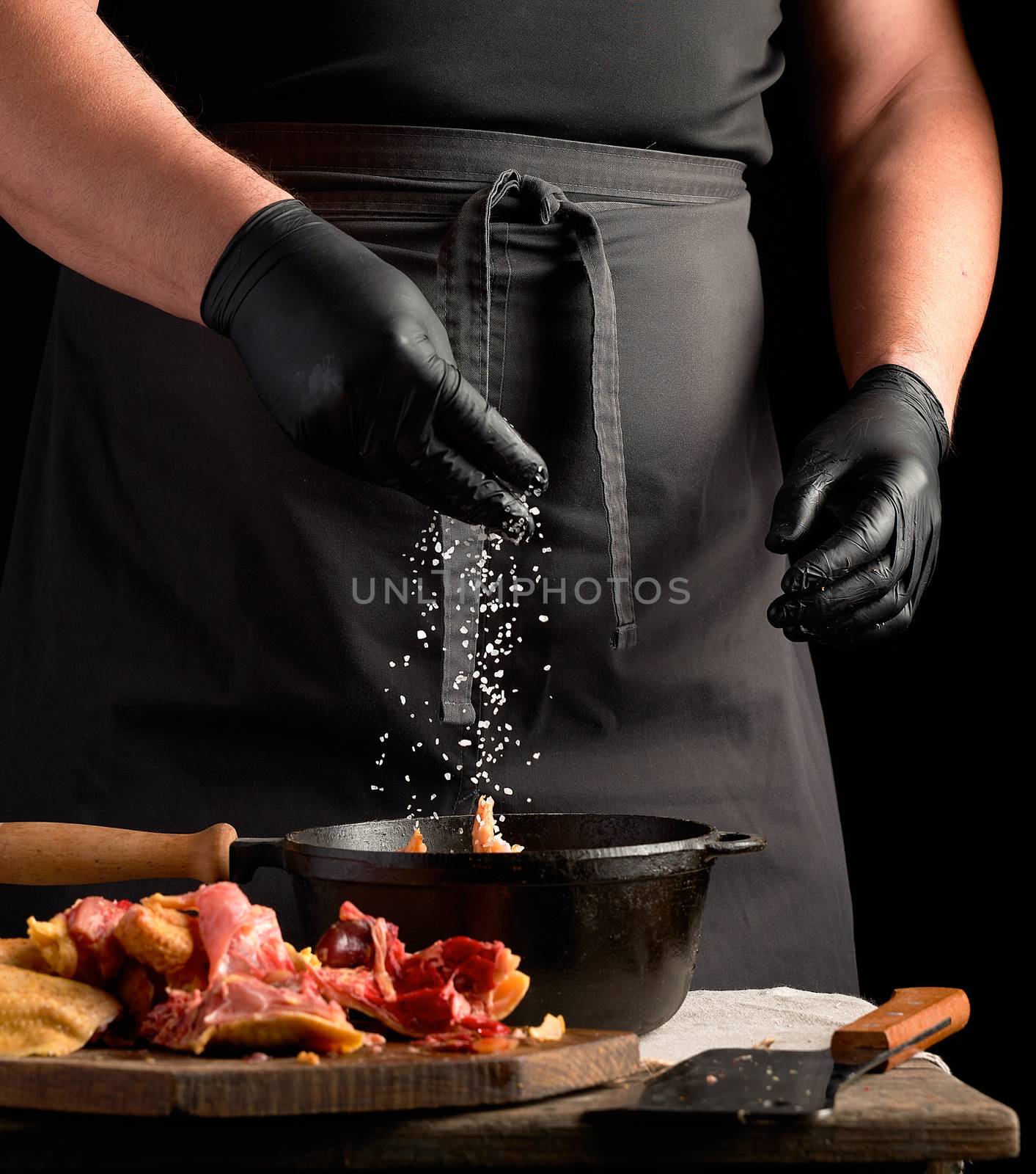 chef in black uniform and latex gloves sprinkles with white salt by ndanko