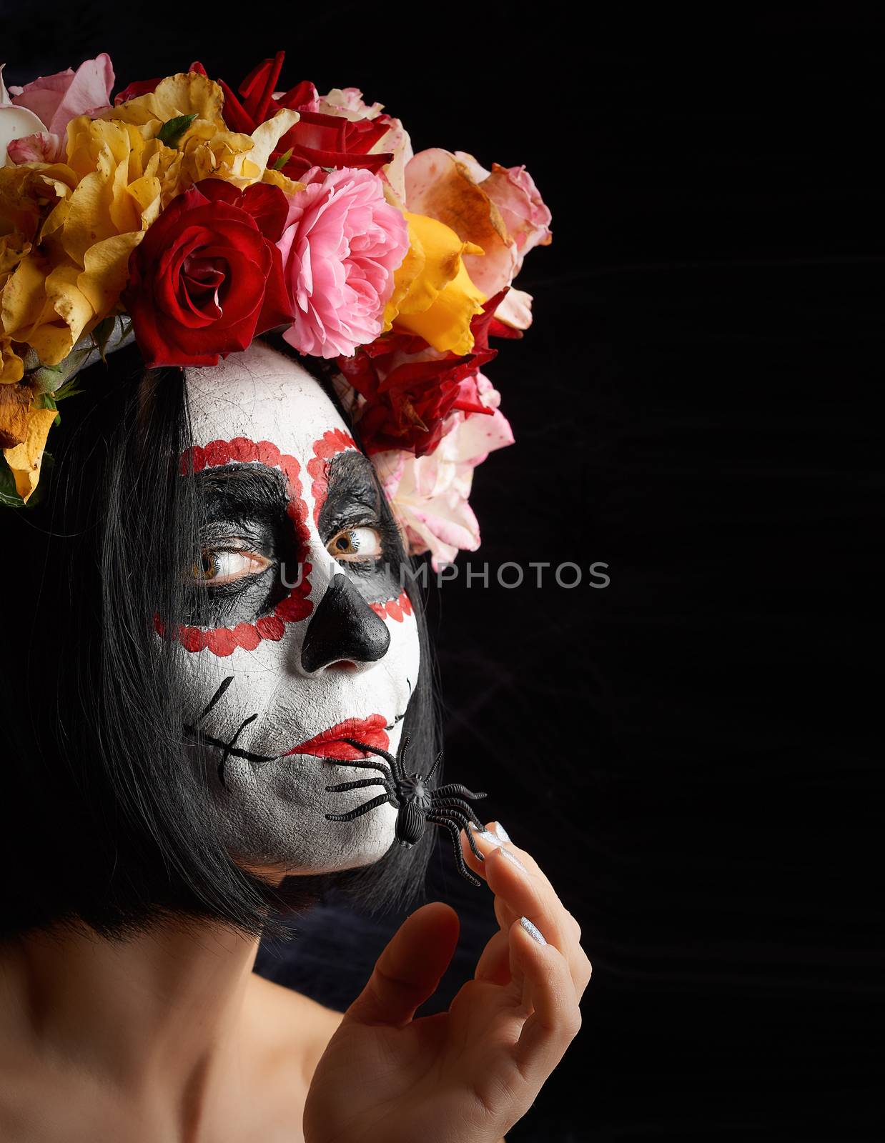 girl with black hair is dressed in a wreath of multi-colored roses and makeup is made on her face Sugar skull to the day of the Dead. Woman looking at the camera 