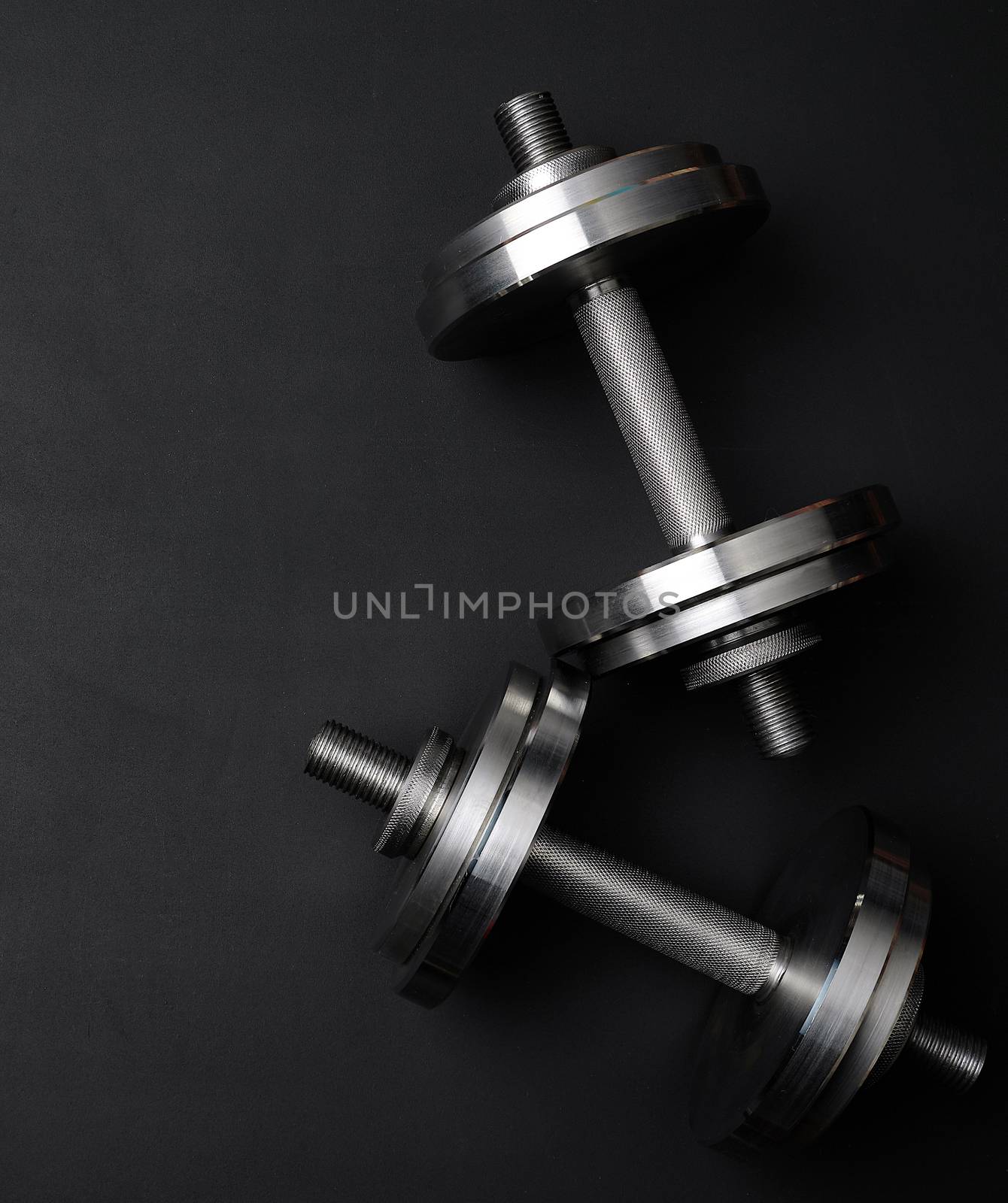 pair of shiny steel typesetting dumbbells for bodybuilding on a black background, top view