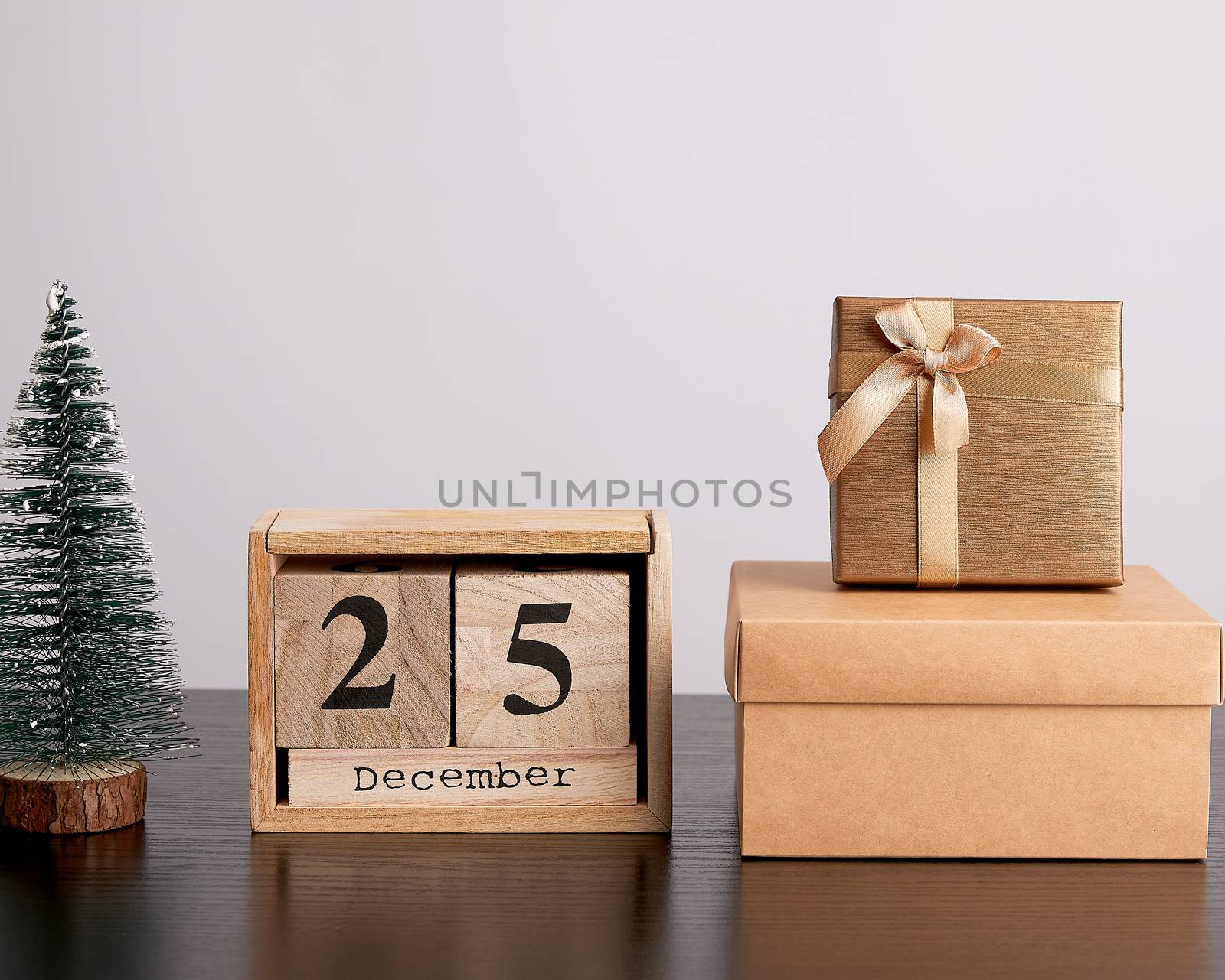 wooden retro calendar from blocks with the date of December 25, Christmas decorative tree and cardboard boxes with gifts, white background