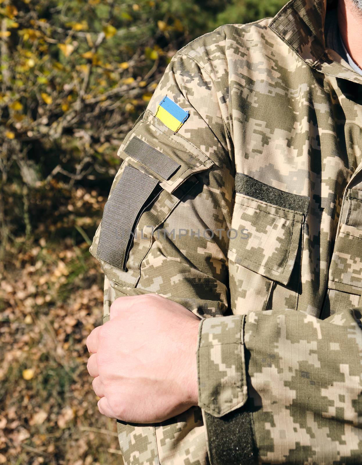 fragment of the hand of a Ukrainian soldier in military camouflage uniform with a patch of the Ukrainian flag, close up