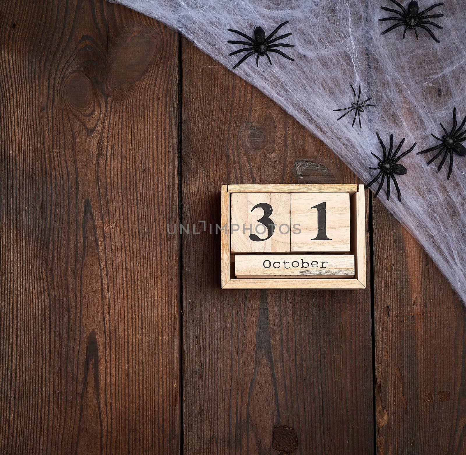 black spider figurines and wooden retro clock made of blocks with the date of October 31 on a brown wooden background, Halloween holiday