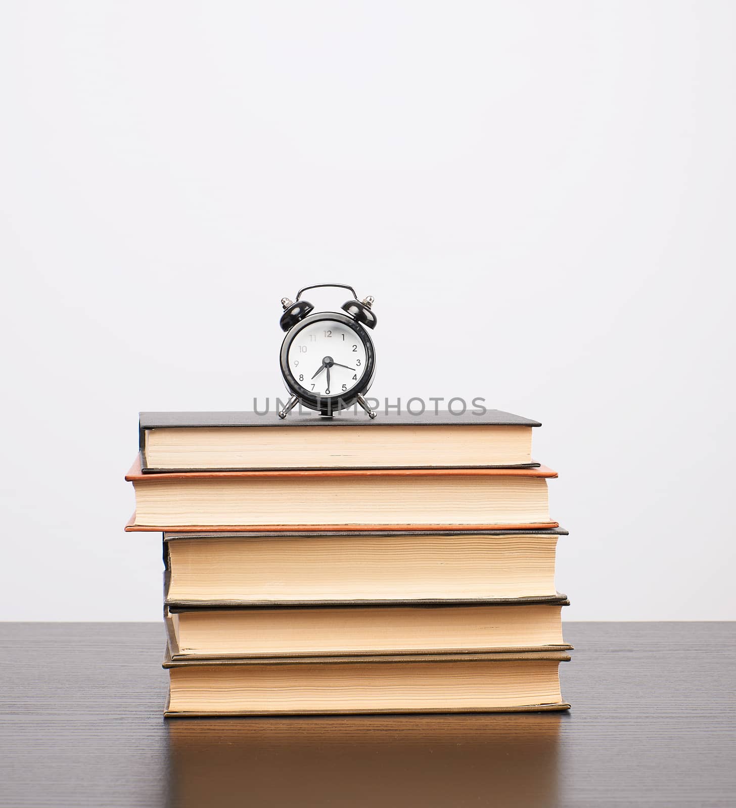 stack of books and a black alarm clock on the table, white background, copy space