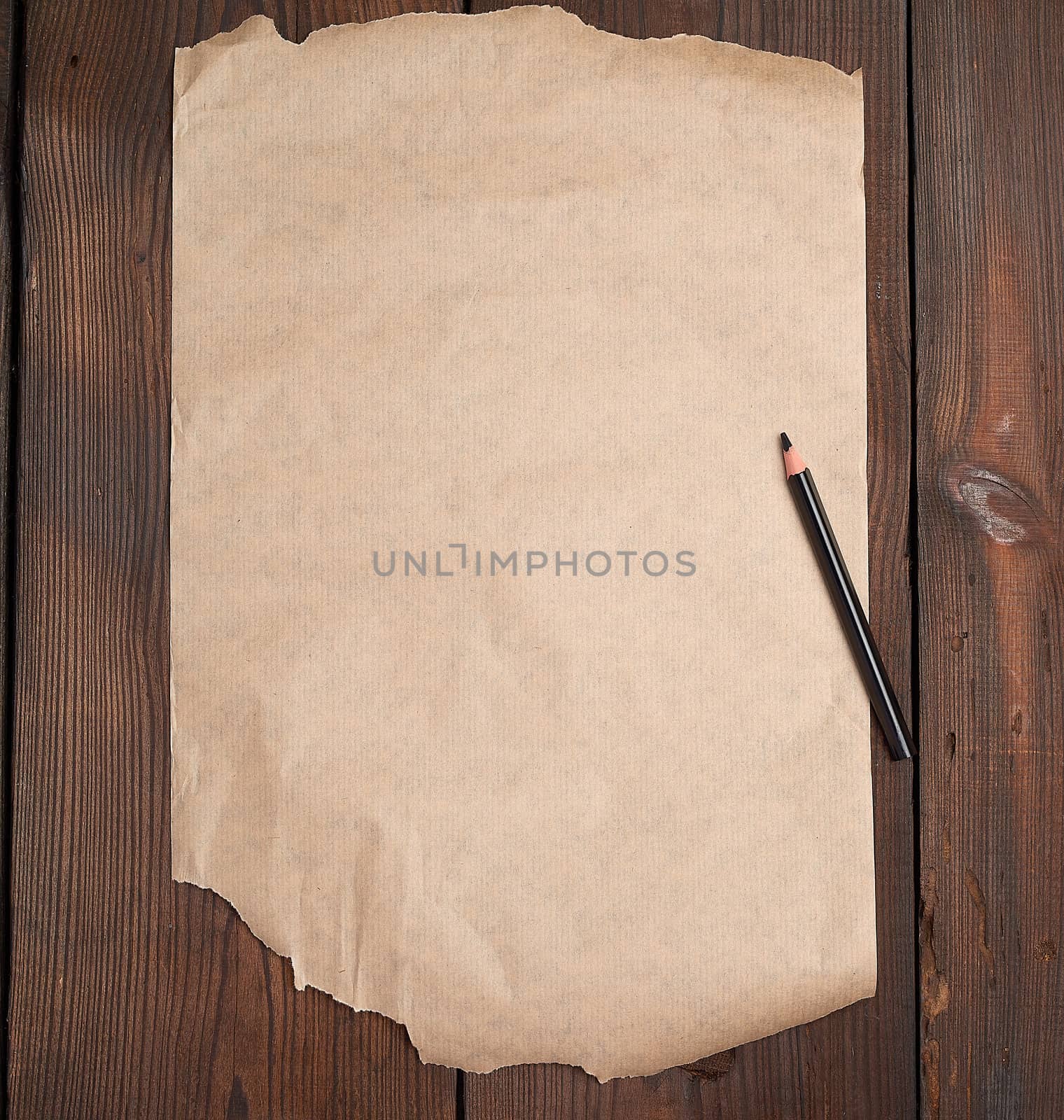 torn empty sheet of brown paper and a black pencil on a wooden surface from old boards, copy space