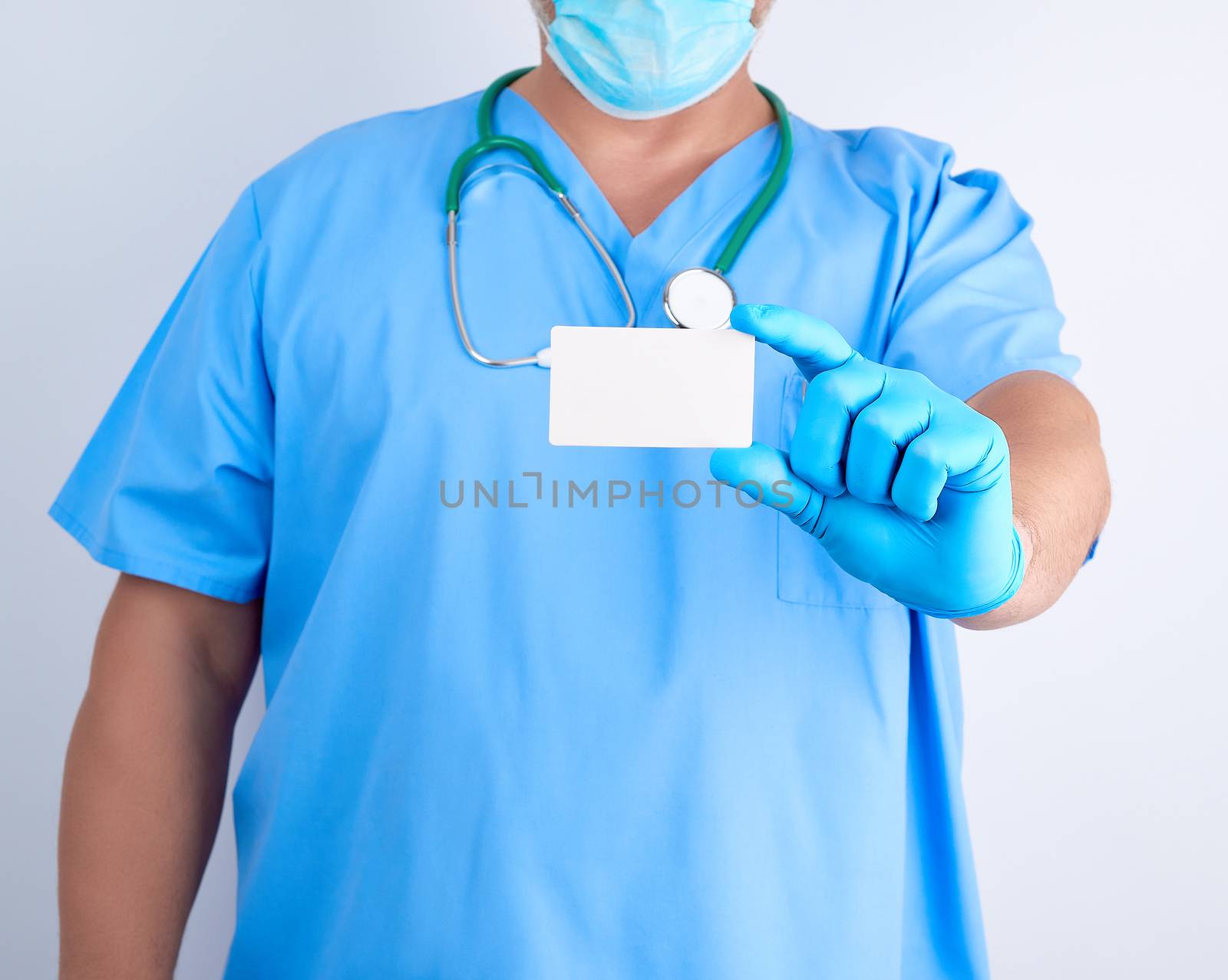 doctor in sterile latex gloves and blue uniform holds a blank white business card, template for the inscription of contacts