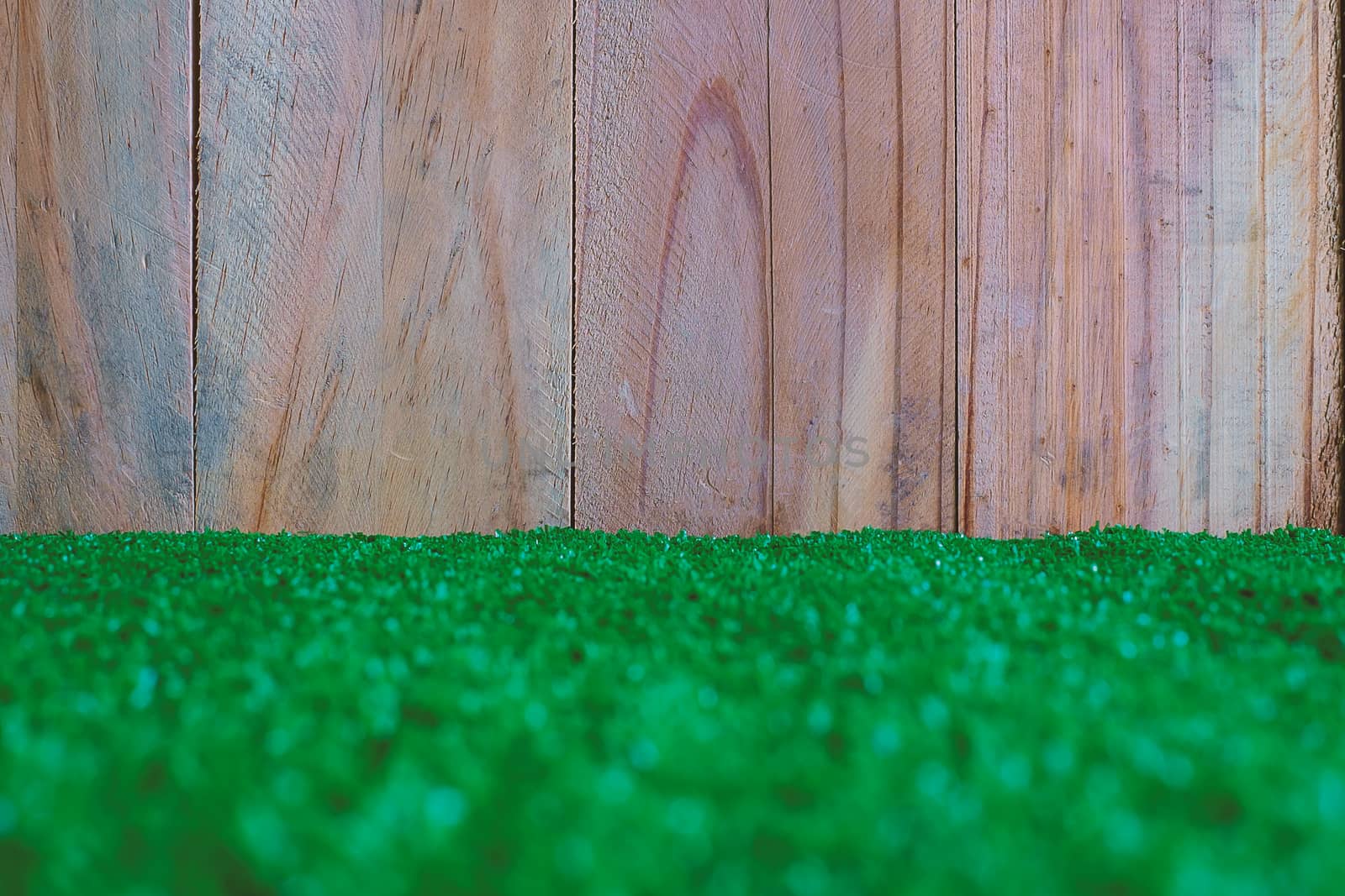The plastic artificial green grass with wooden wall for background