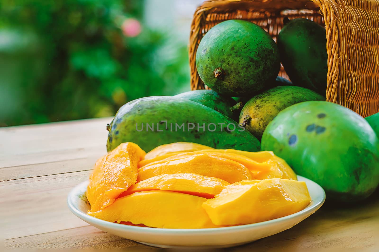 Ripe mango fruit in the basket on wooden table with blurred green background, selective focus