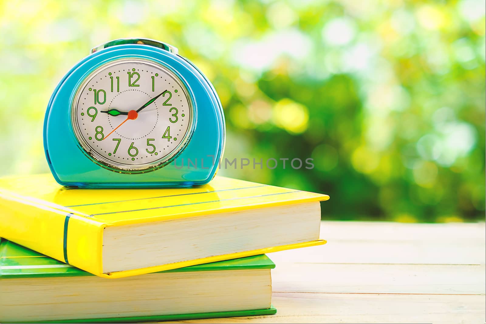 Old blue alarm clock on books with blurred green natural background