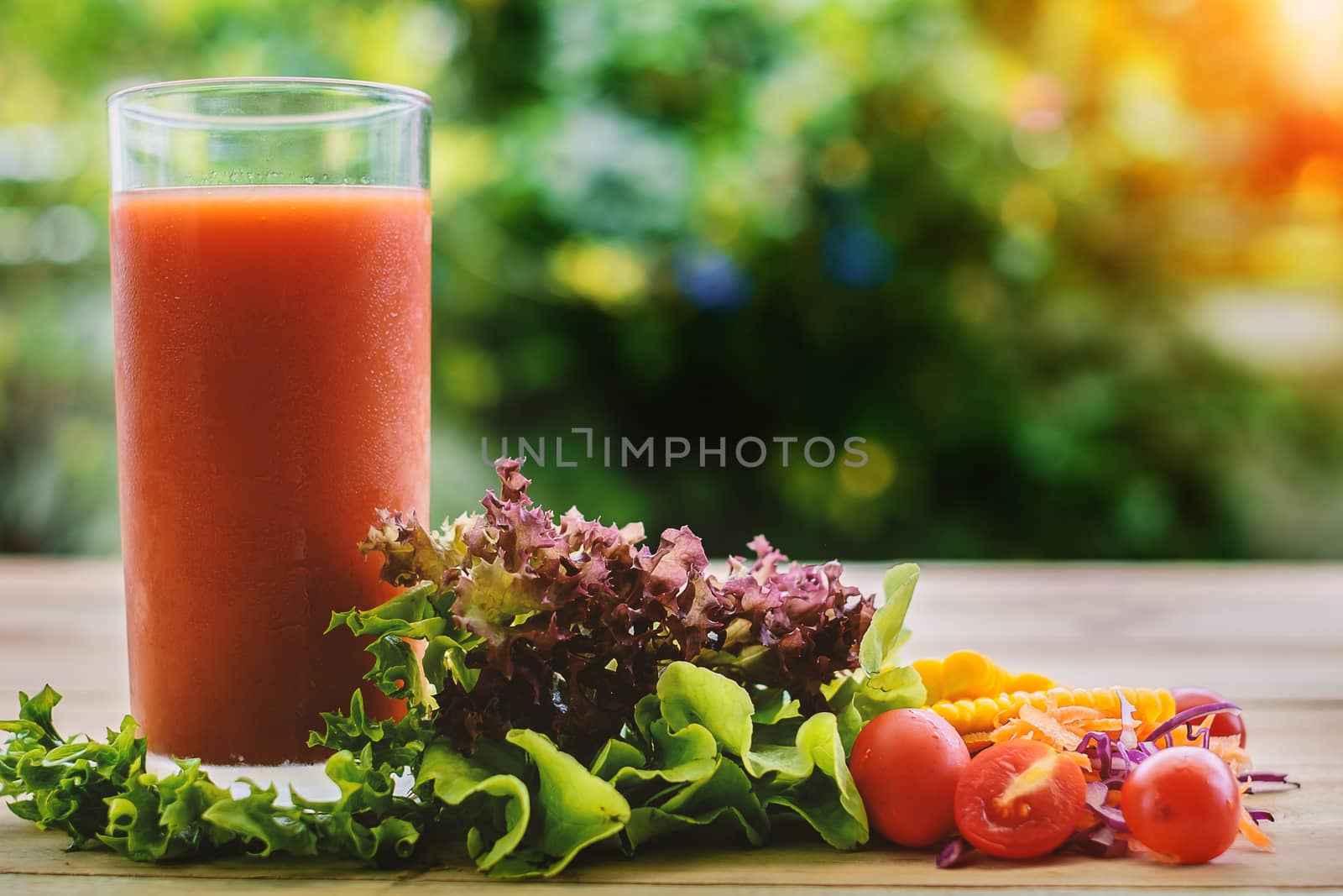 A glass of vegetable juice on wooden table with blurred natural green background