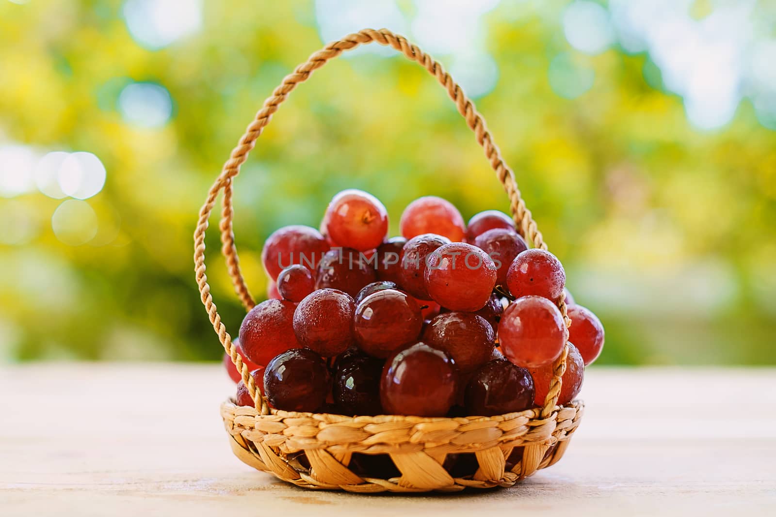 Red grape fruit in the basket on the wooden table with the natural blurred background