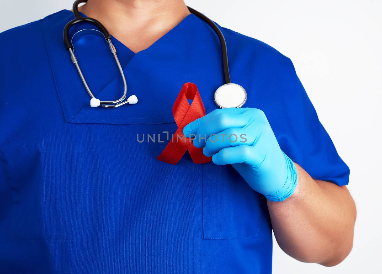 doctor in blue uniform and sterile latex gloves holds a red ribbon - a symbol of the fight against disease AIDS and vasculitis