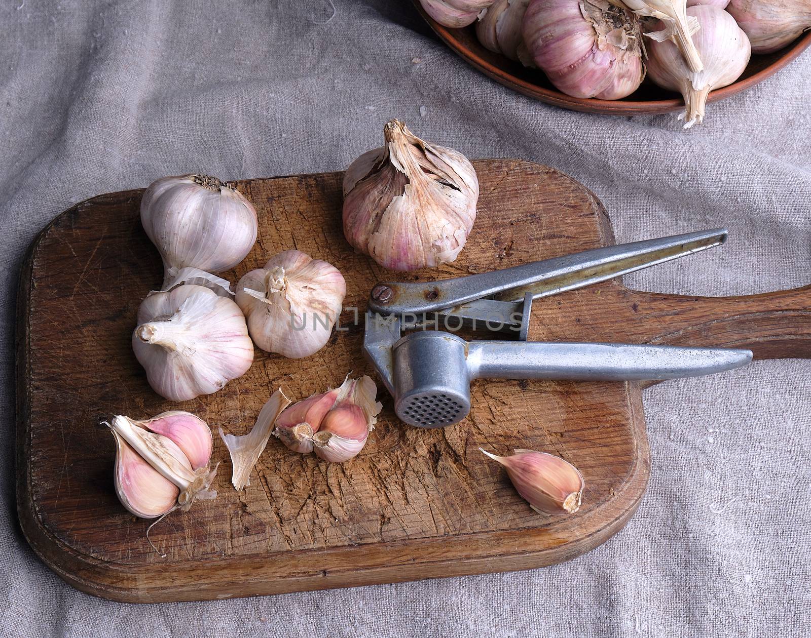 raw unpeeled garlic on a very old vintage cutting board and an iron extruder for a product, dark background