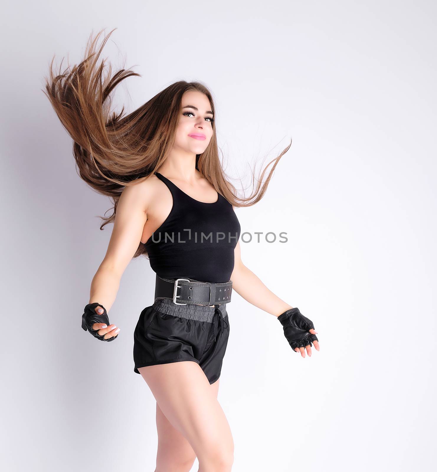 beautiful girl with a sports figure stands on a white background and throws up dark long blonde hair with her hands, athlete is dressed in short shorts and a black top, white background
