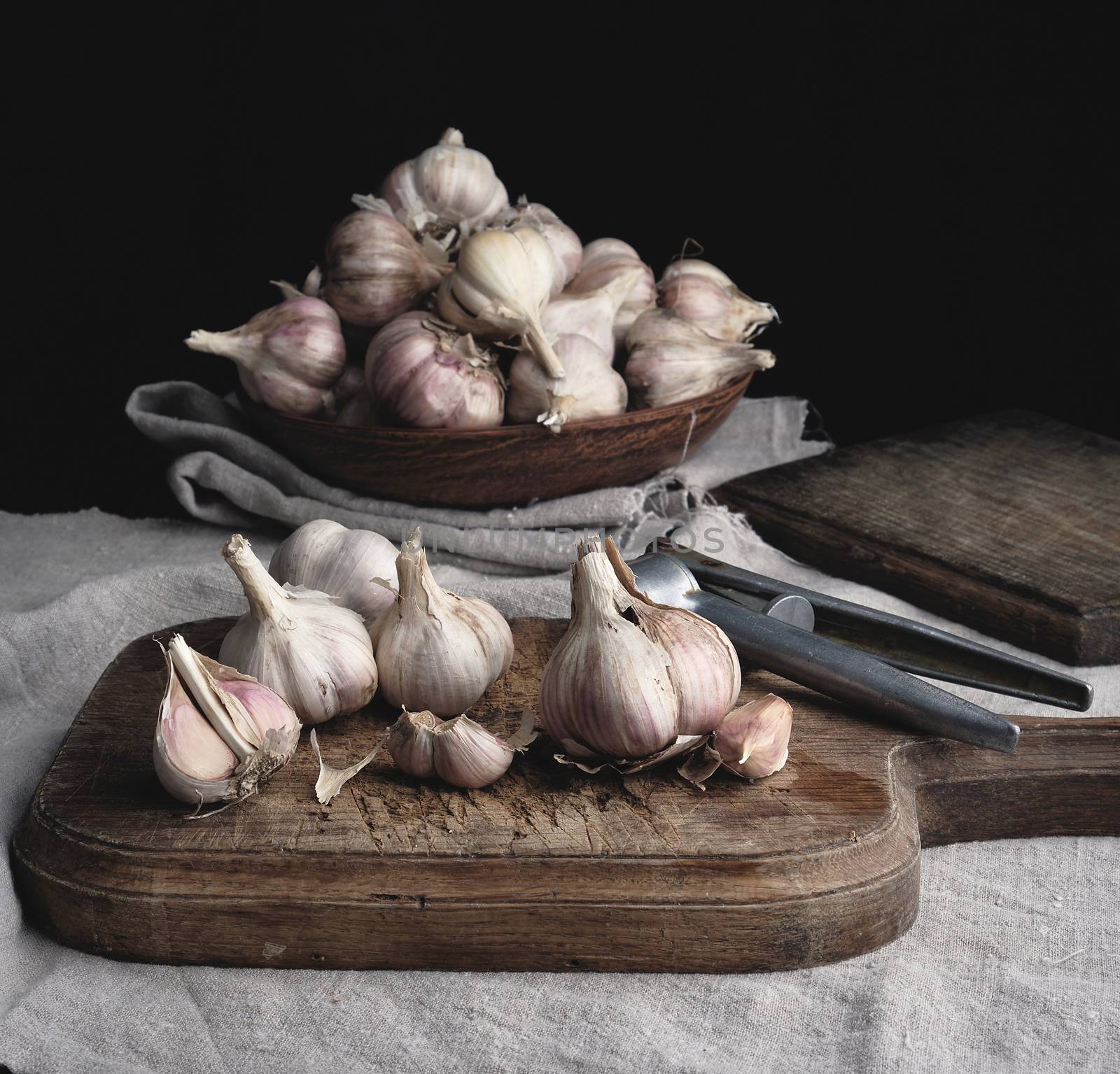 raw unpeeled garlic on a very old vintage cutting board and iron pres, dark background