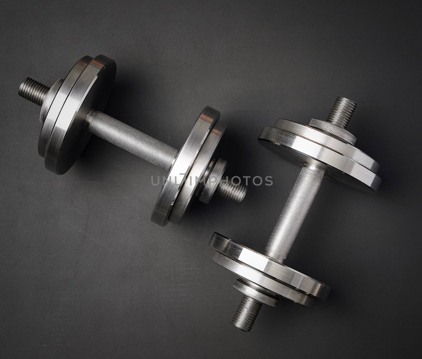 pair of shiny steel typesetting dumbbells for bodybuilding on a black background, top view