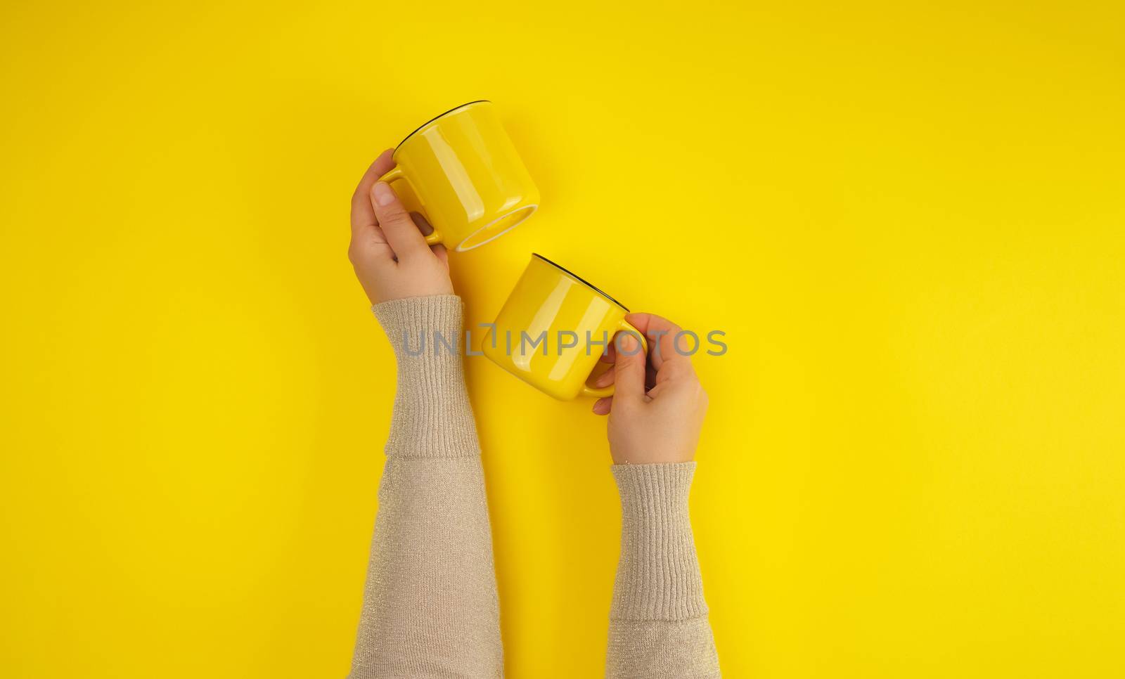two yellow ceramic cups are supported by a female hand on a yellow background, copy space