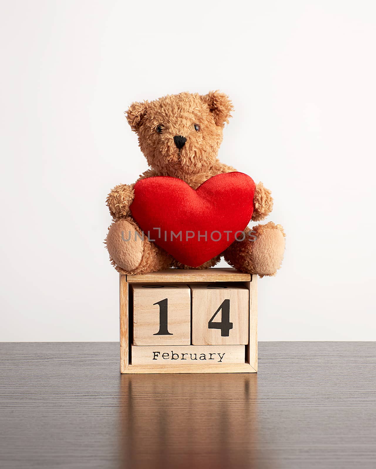 wooden calendar of cubes with the date of February 14 and a brown teddy bear on a black table, Valentine's Day celebration