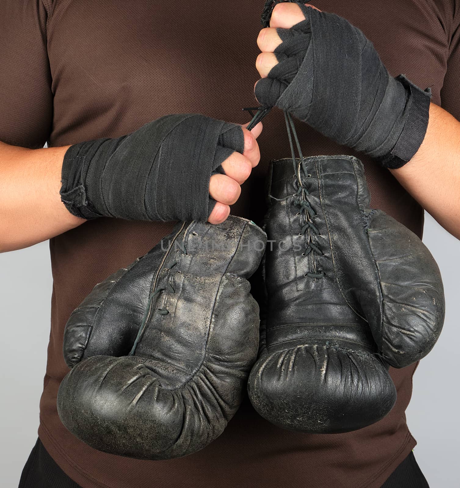 athlete in brown clothes holds very old black vintage leather boxing gloves, white background, close up 