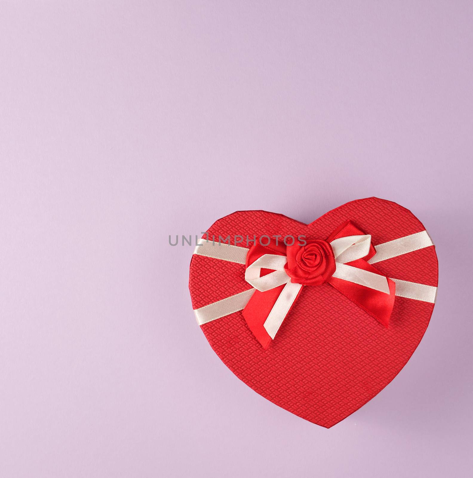 closed red gift box in the form of a heart with a bow on a purple background, copy space