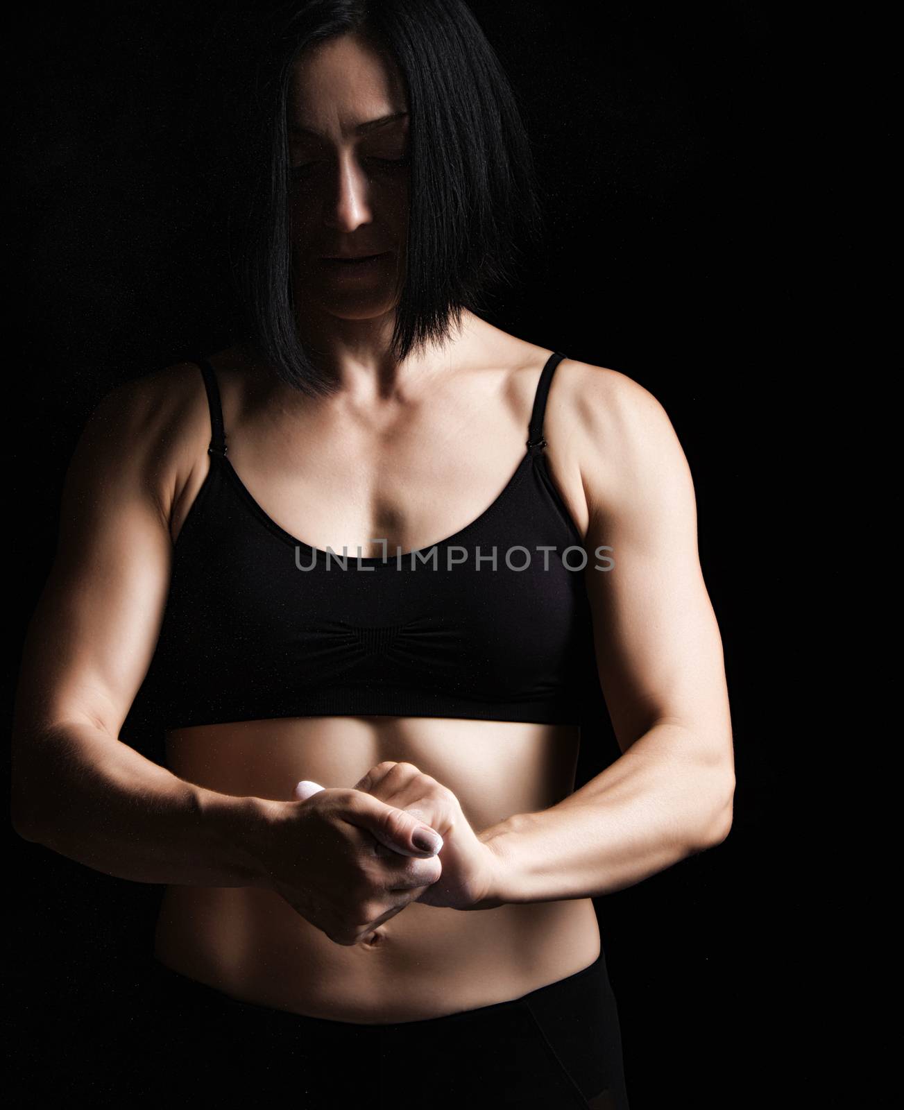 beautiful young girl with a sports figure dressed in a black top claps in her hands with white magnesia, preparing before exercise, low key