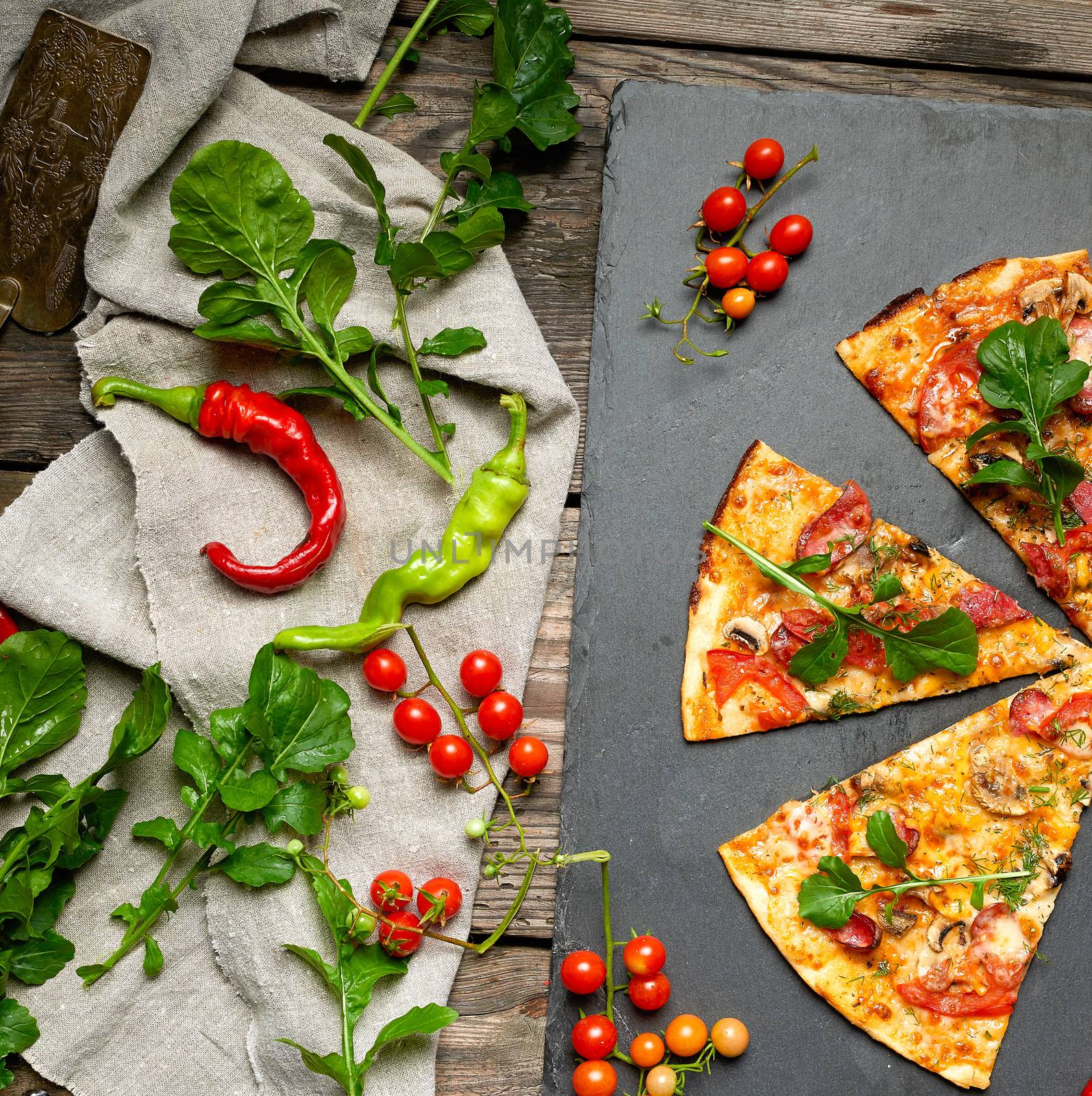 baked round pizza with smoked sausages, mushrooms, tomatoes, cheese and arugula leaves, food is cut in portions, wooden table 