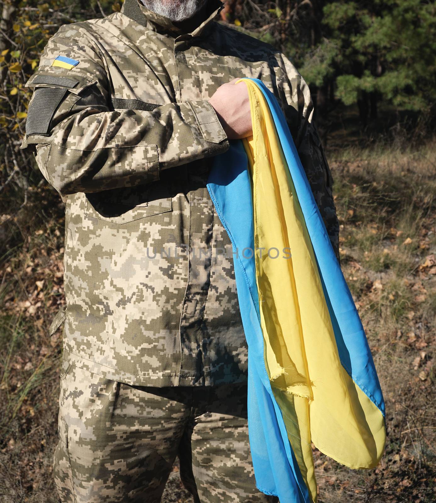 Ukrainian soldier holds in his hand the yellow-blue flag of the state, he pressed his hand to his chest, concept of the memory of the dead soldiers