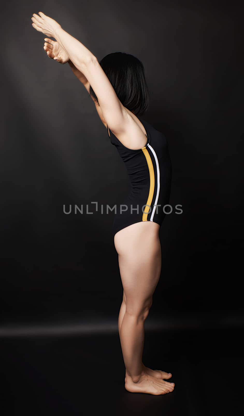 Adult girl with a sports figure standing on a dark background, muscular body, black hair, low key