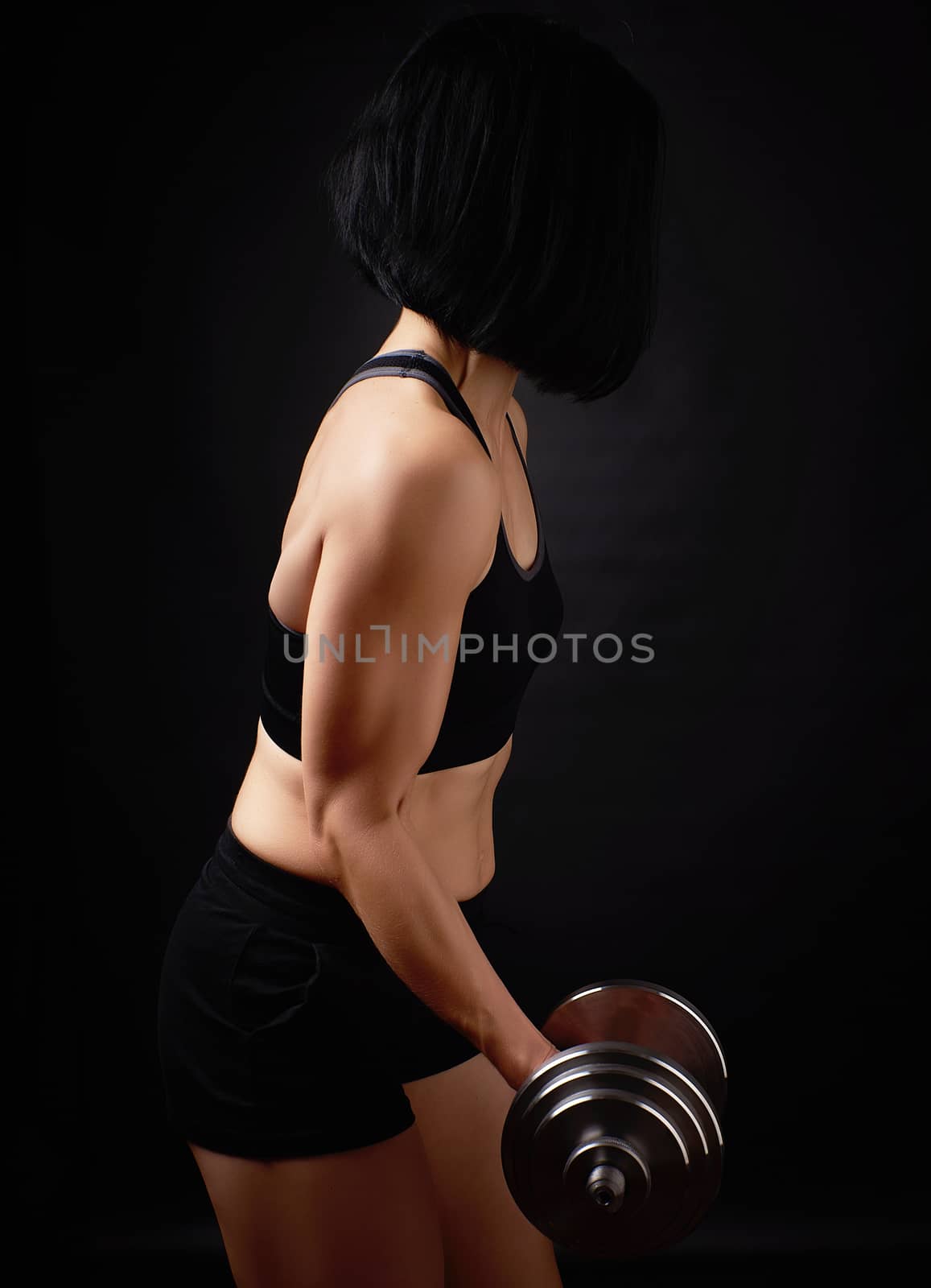 young woman of Caucasian appearance holds steel type-setting dumbbells in her hands, sports training, dark background