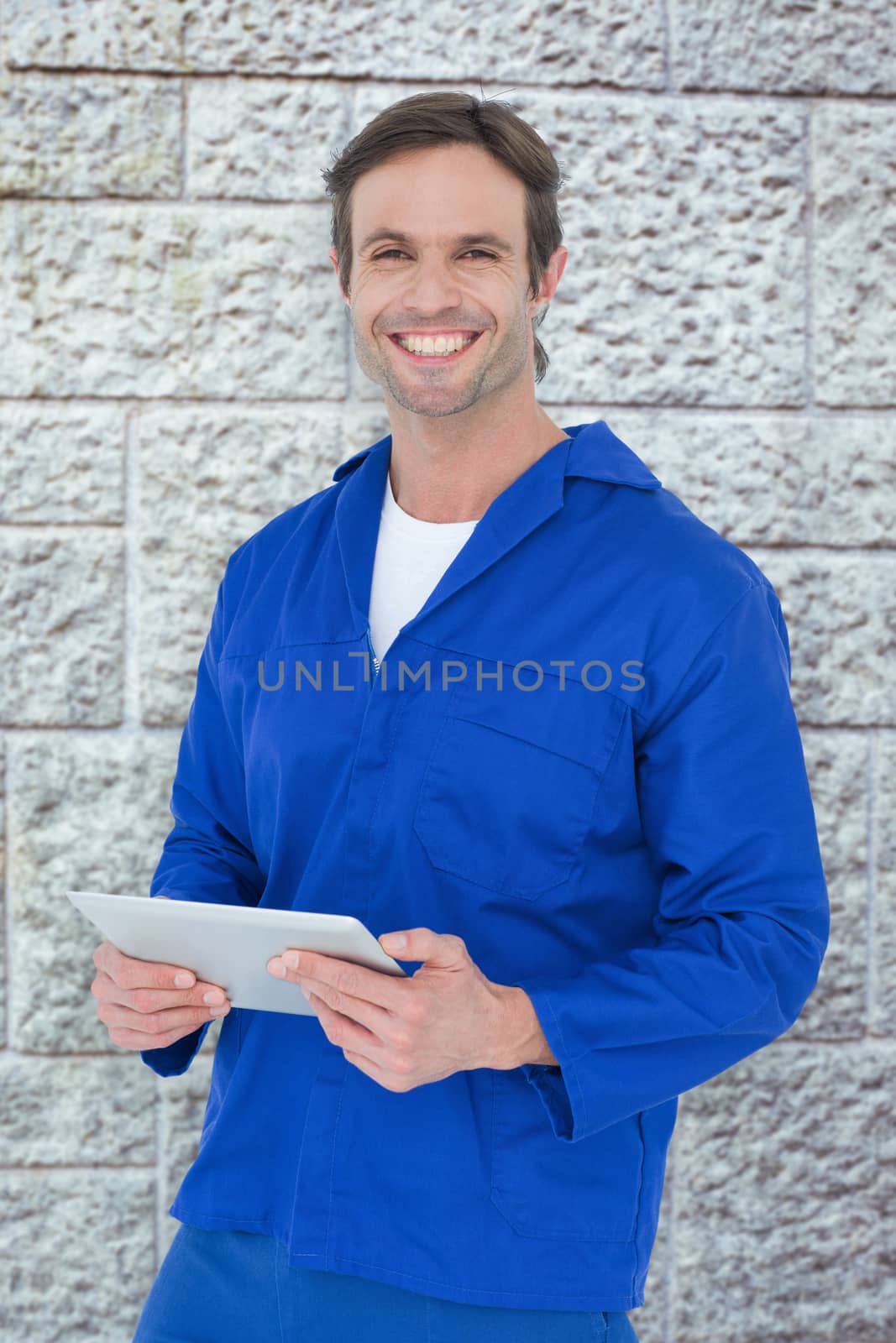 Handsome mechanic holding digital tablet against grey brick wall