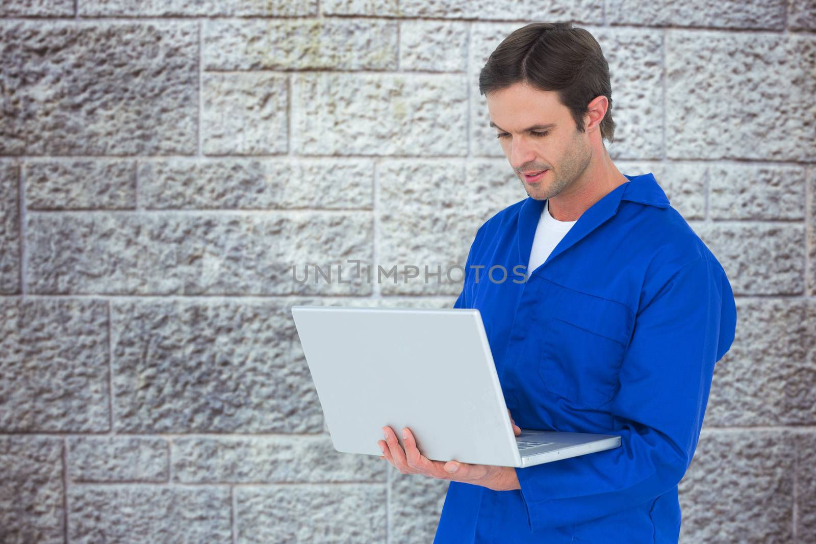 Mechanic using laptop over white background against grey brick wall