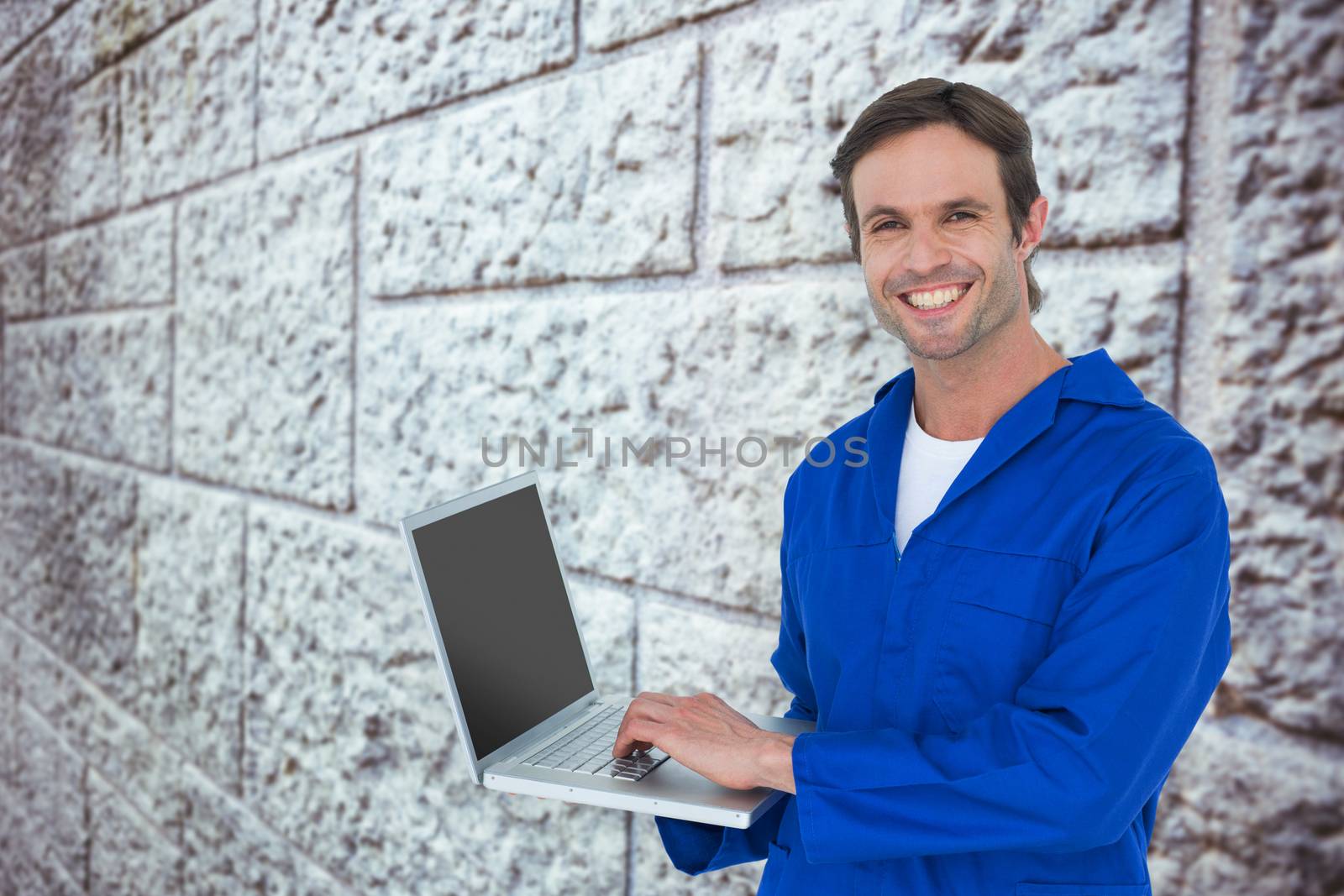 Handsome mechanic using laptop over white background against grey brick wall