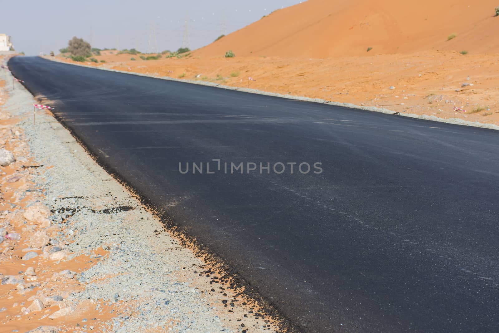 New ashphalt road in the desert sand with no cars or people. Contruction, desolate, hot, arid concepts.