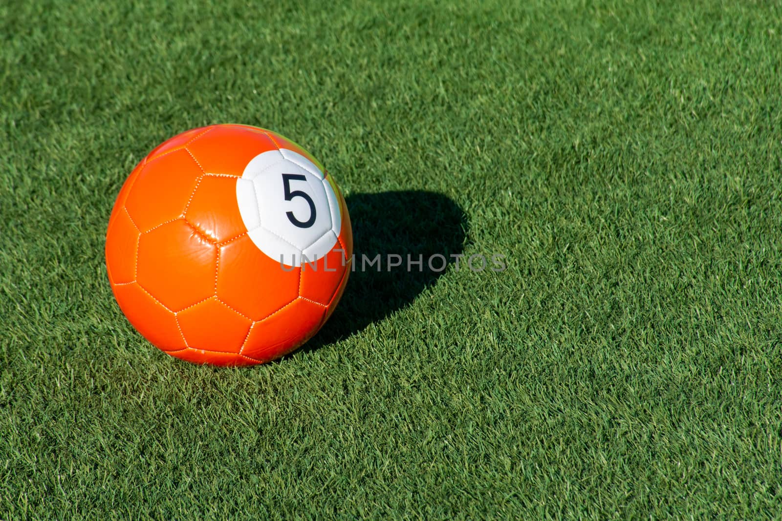 Bright orange number 5 soccer billiards or pool ball on green gr by kingmaphotos