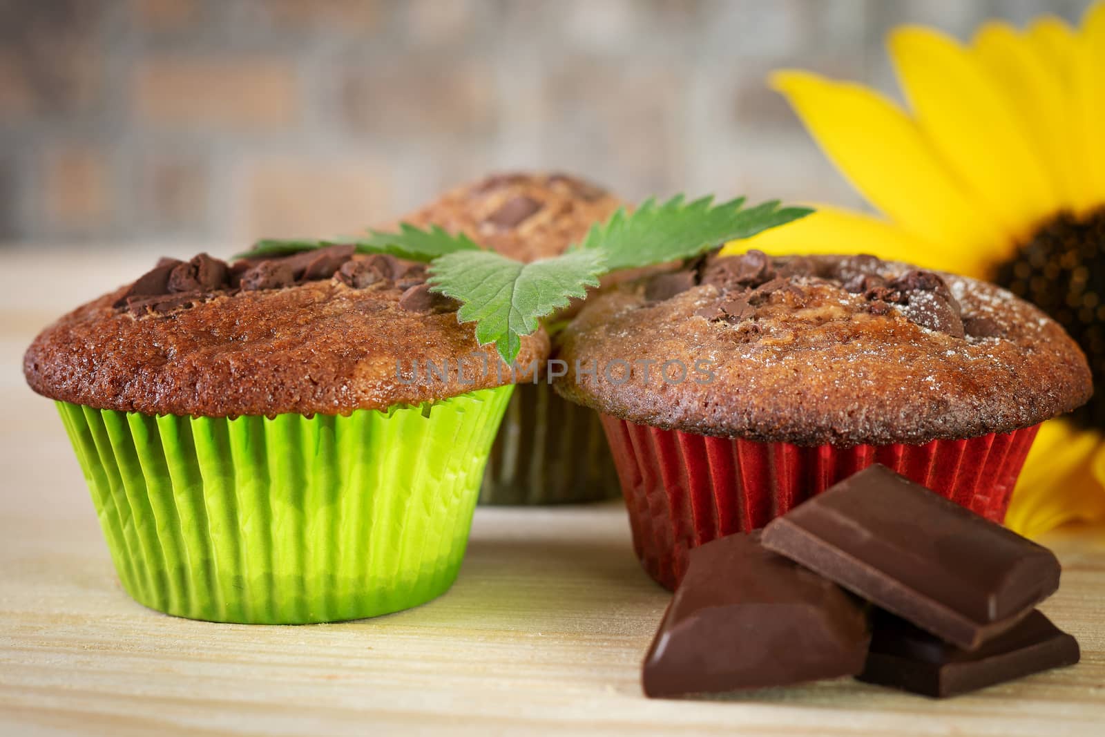 Muffins in colorful baskets with chocolate and sunflower on wooden table. Close up. Blurred foreground and background.