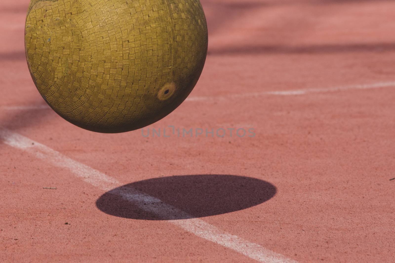 Yellow four square playground ball bouncing on red court with shadow. Exercise, fitness and fun concept.