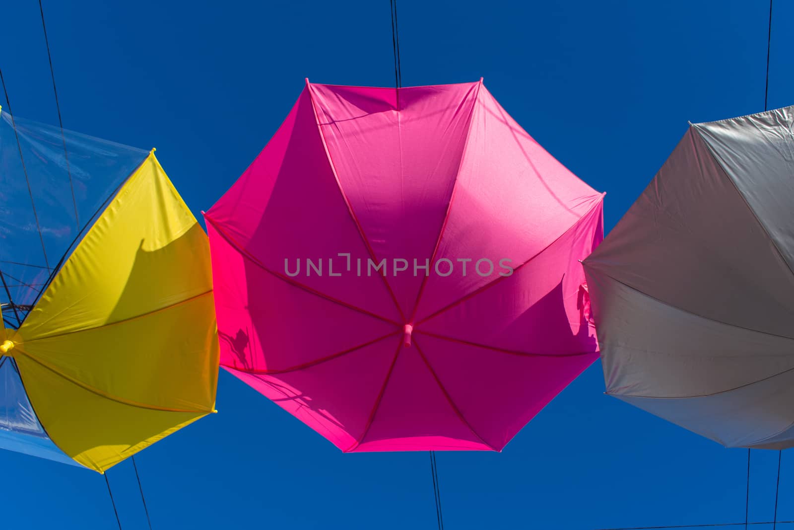Colorful vibrant umbrellas hanging over the walking street for a festival on a blue sky sunny day close up of the pink umbrella.