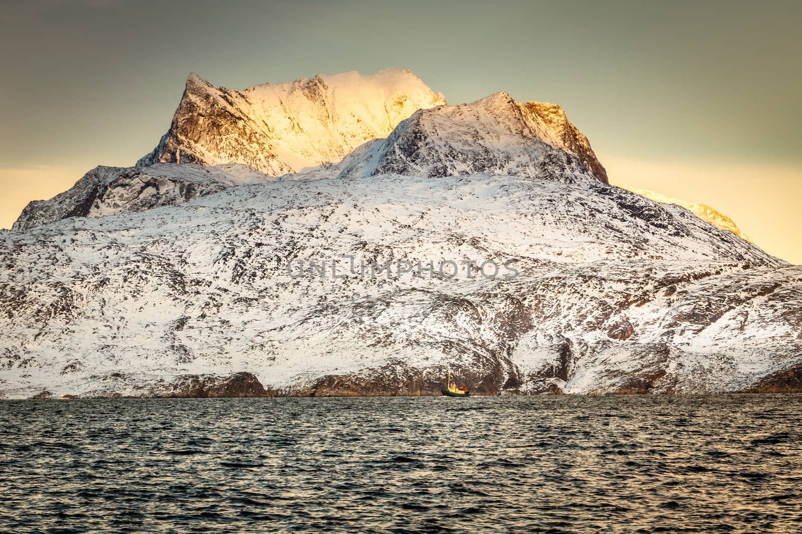 Huge Sermitsiaq mountain in a sunset rays covered in snow with blue sea and small fishing boat, nearby Nuuk city, Greenland